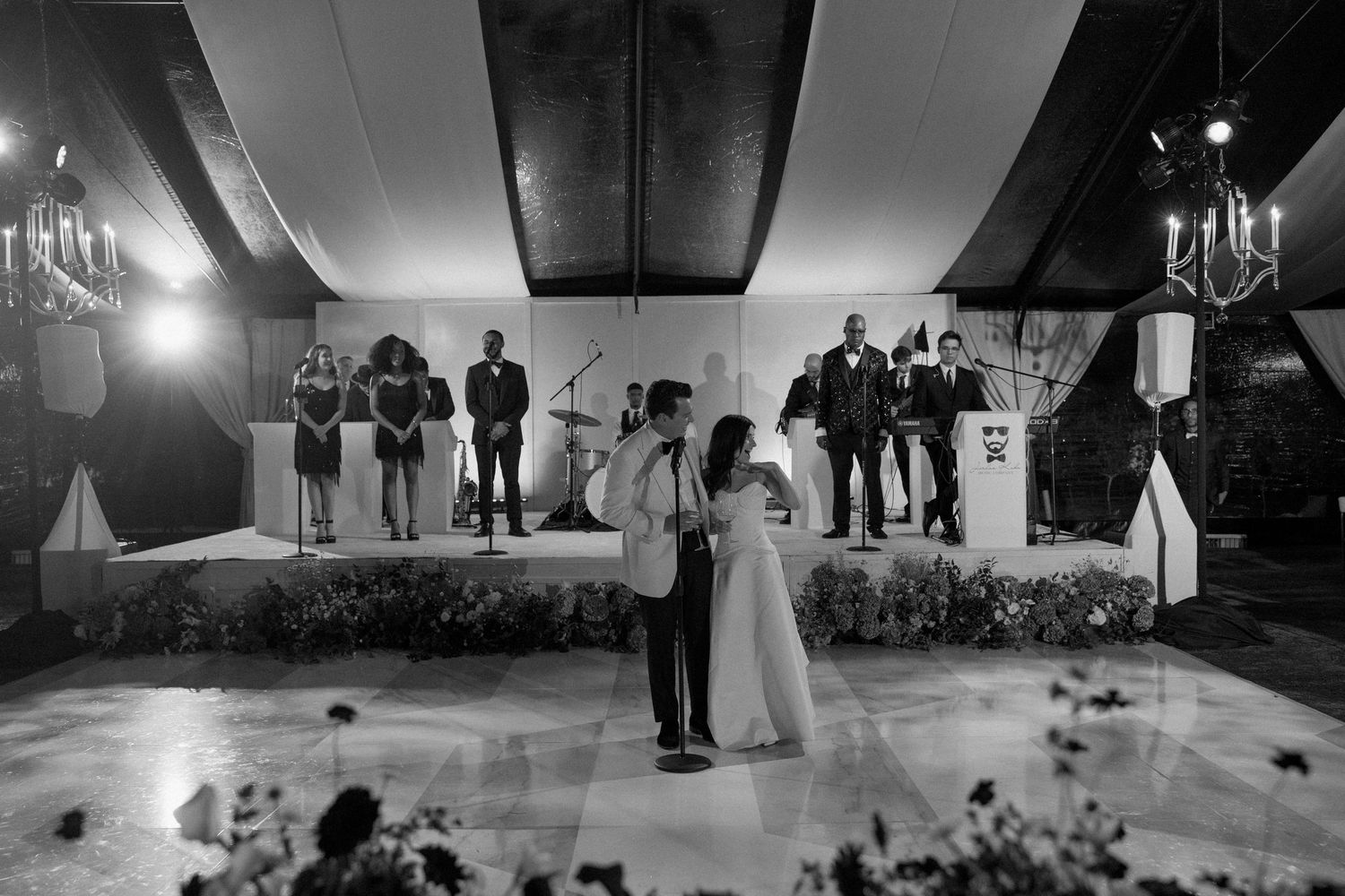 A black and white panoramic view of a wedding reception dance floor with guests celebrating.