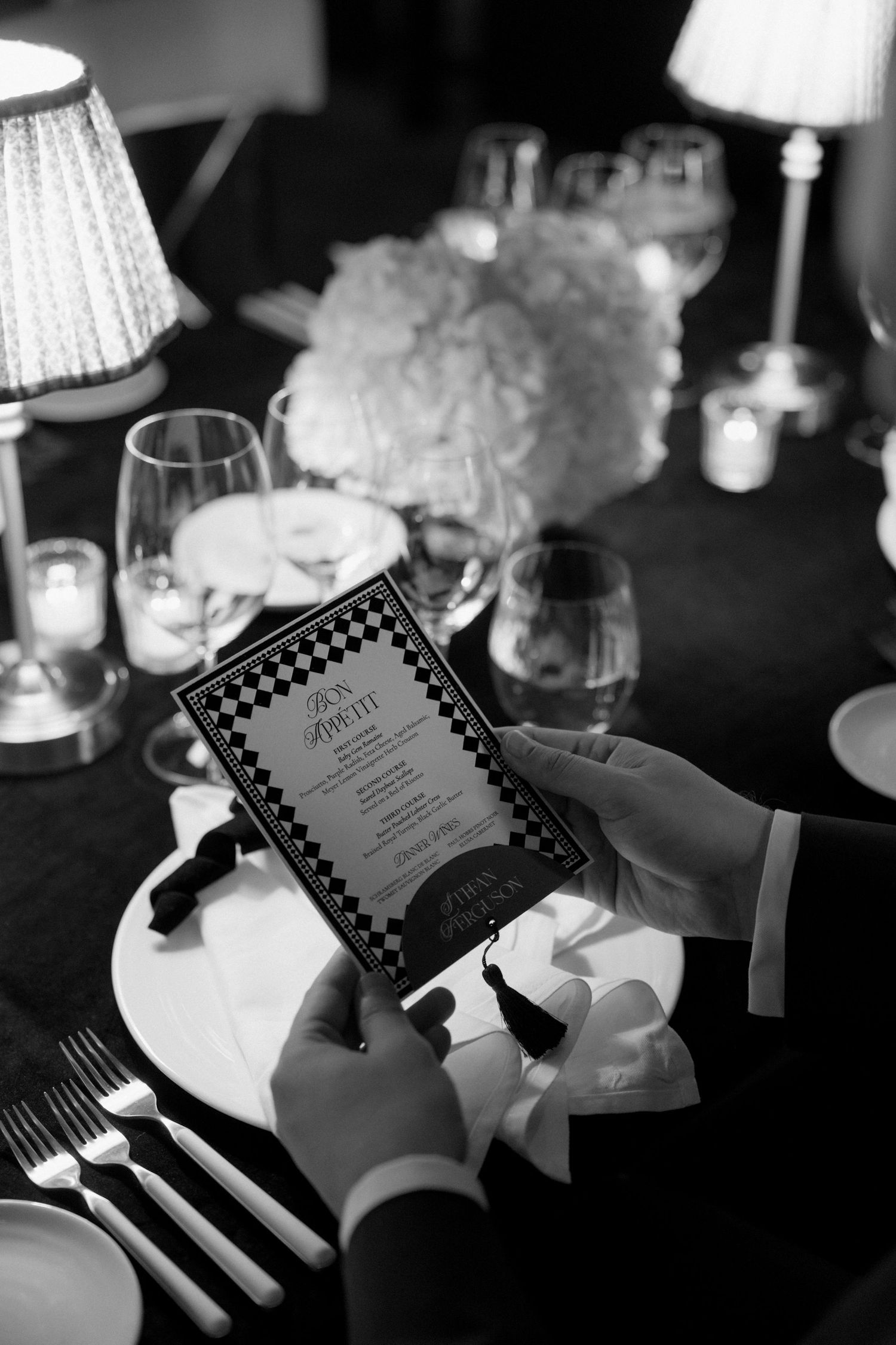 Black and white photo of hands holding a menu at an elegant dinner table setting.