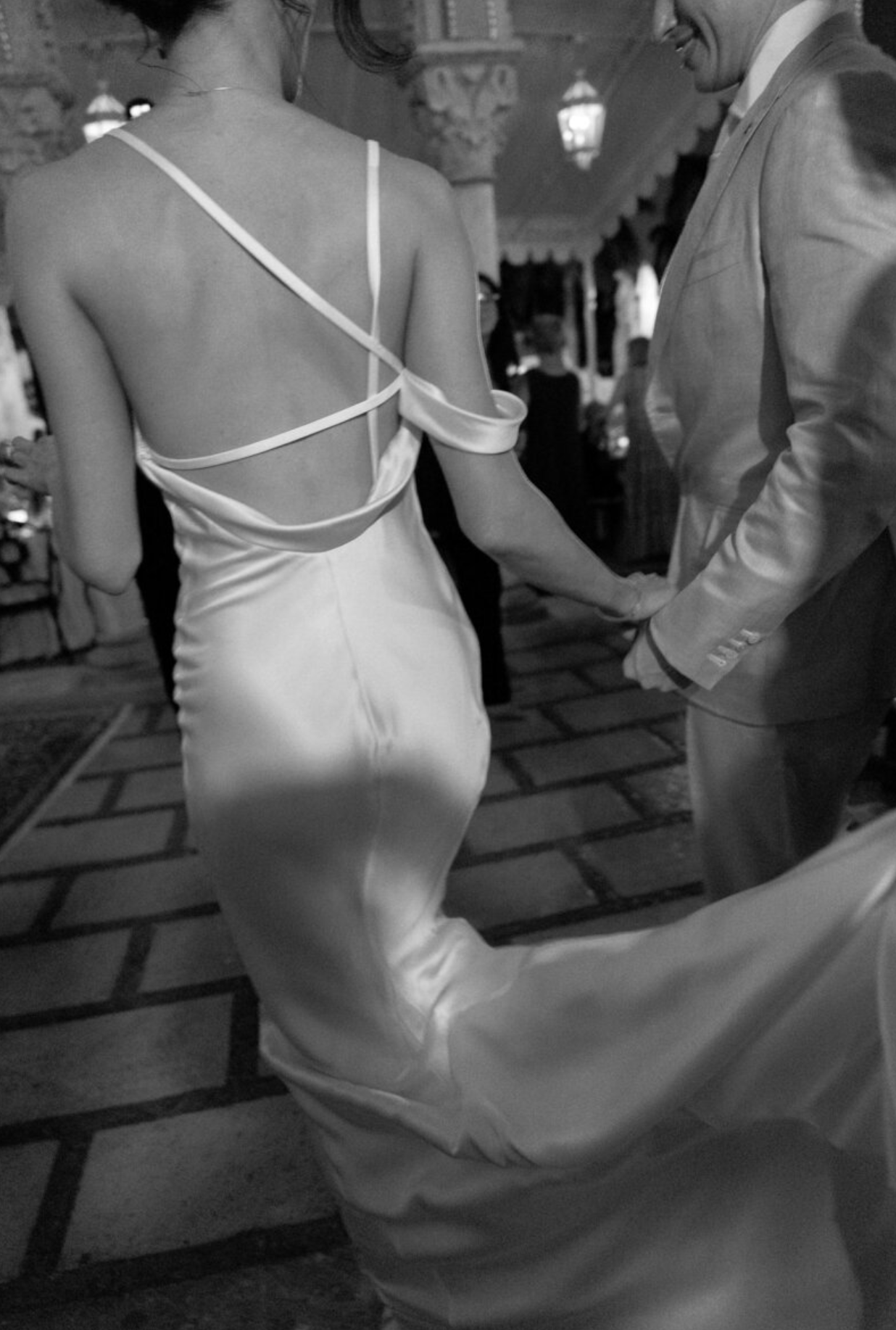 Back view of bride in fitted white dress with intricate straps standing on stone patio.