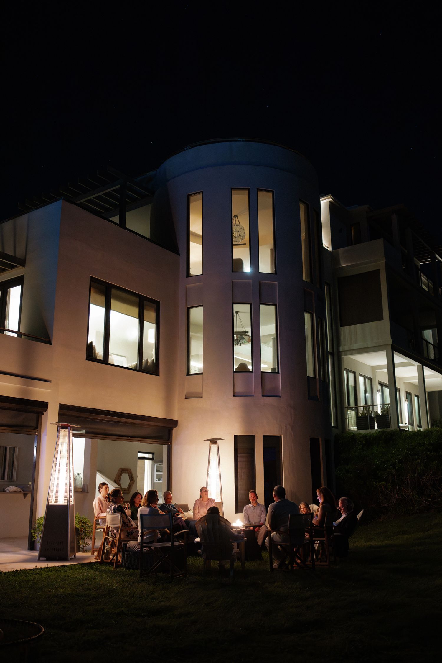 A large, illuminated building with people gathered outside on the lawn at night.
