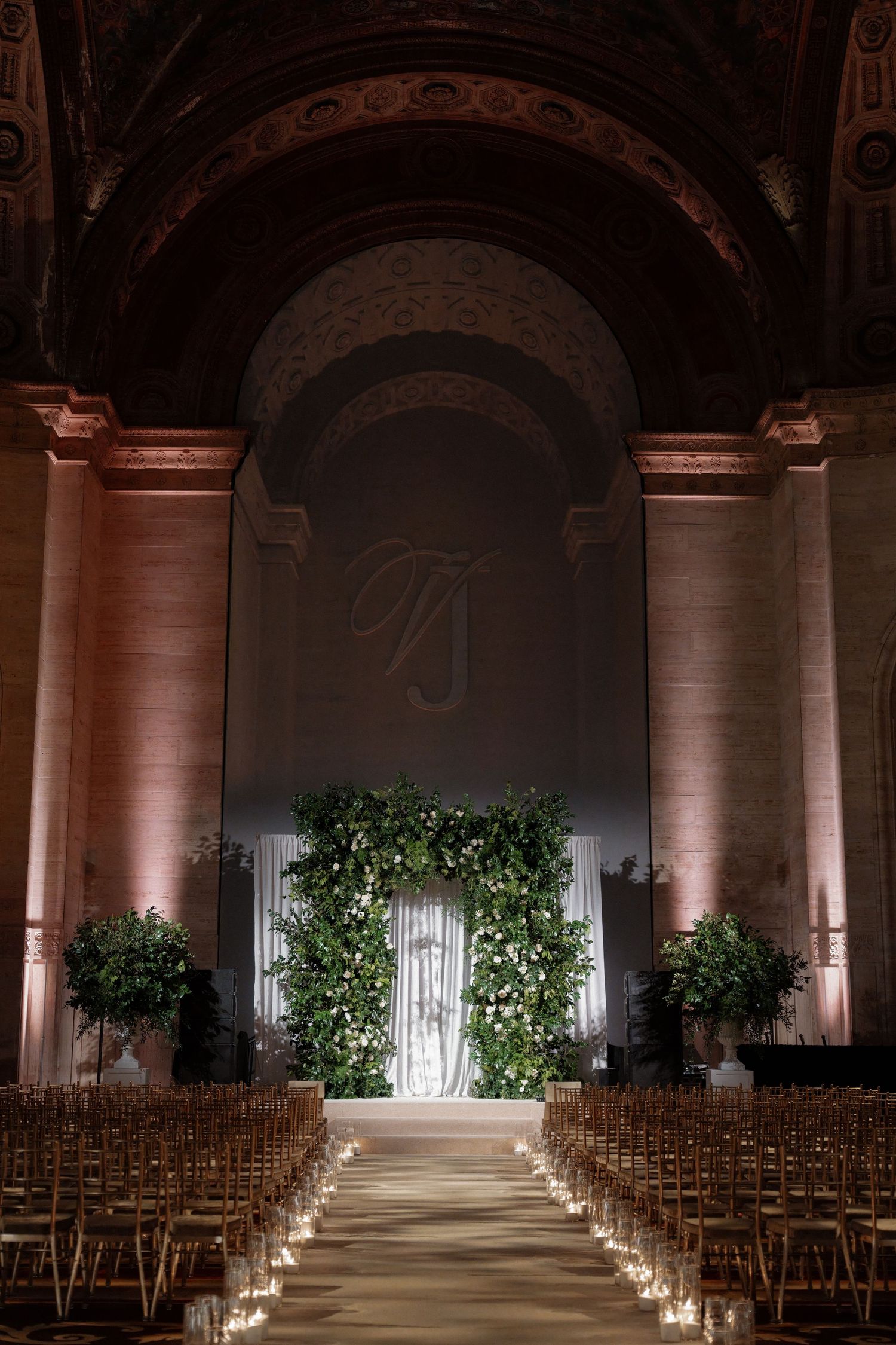 A grand, dimly lit wedding ceremony venue with an aisle lined with candles and floral arrangements.