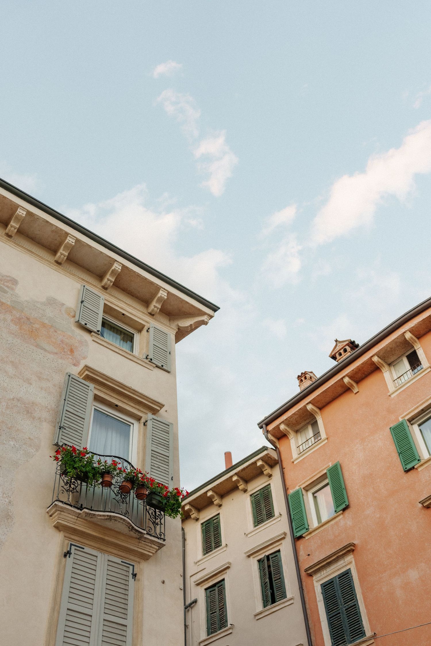 Low angle view of classic European buildings with shuttered windows and flower boxes against blue sky.