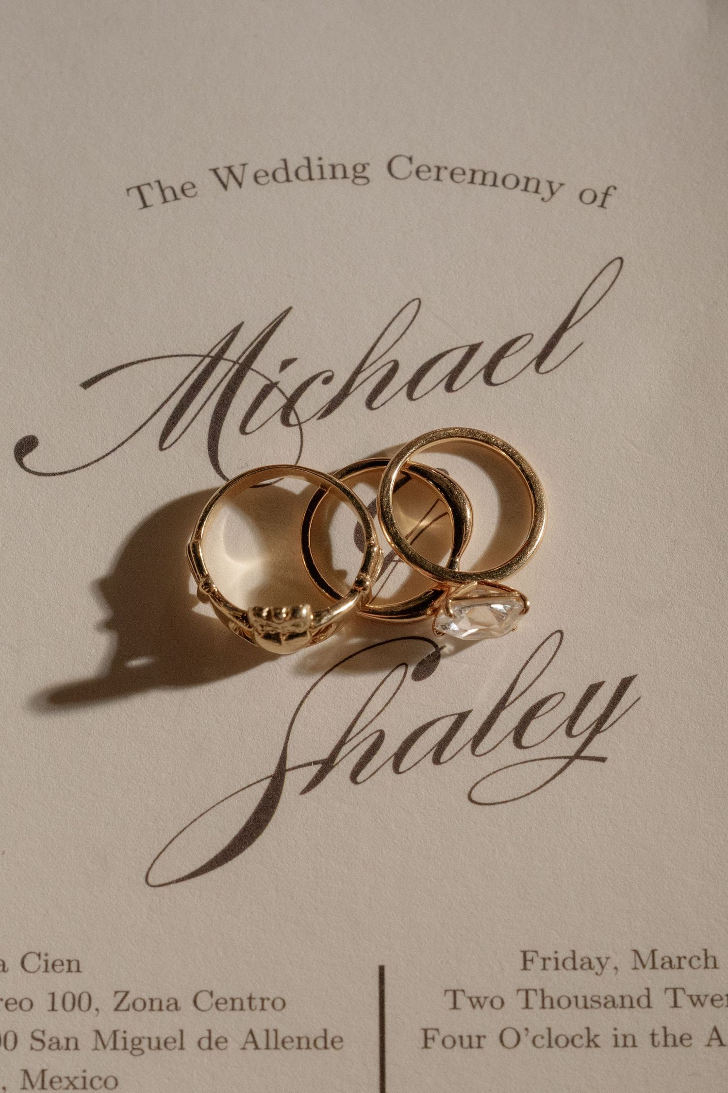 Wedding invitation with gold rings casting shadows on elegant calligraphy.