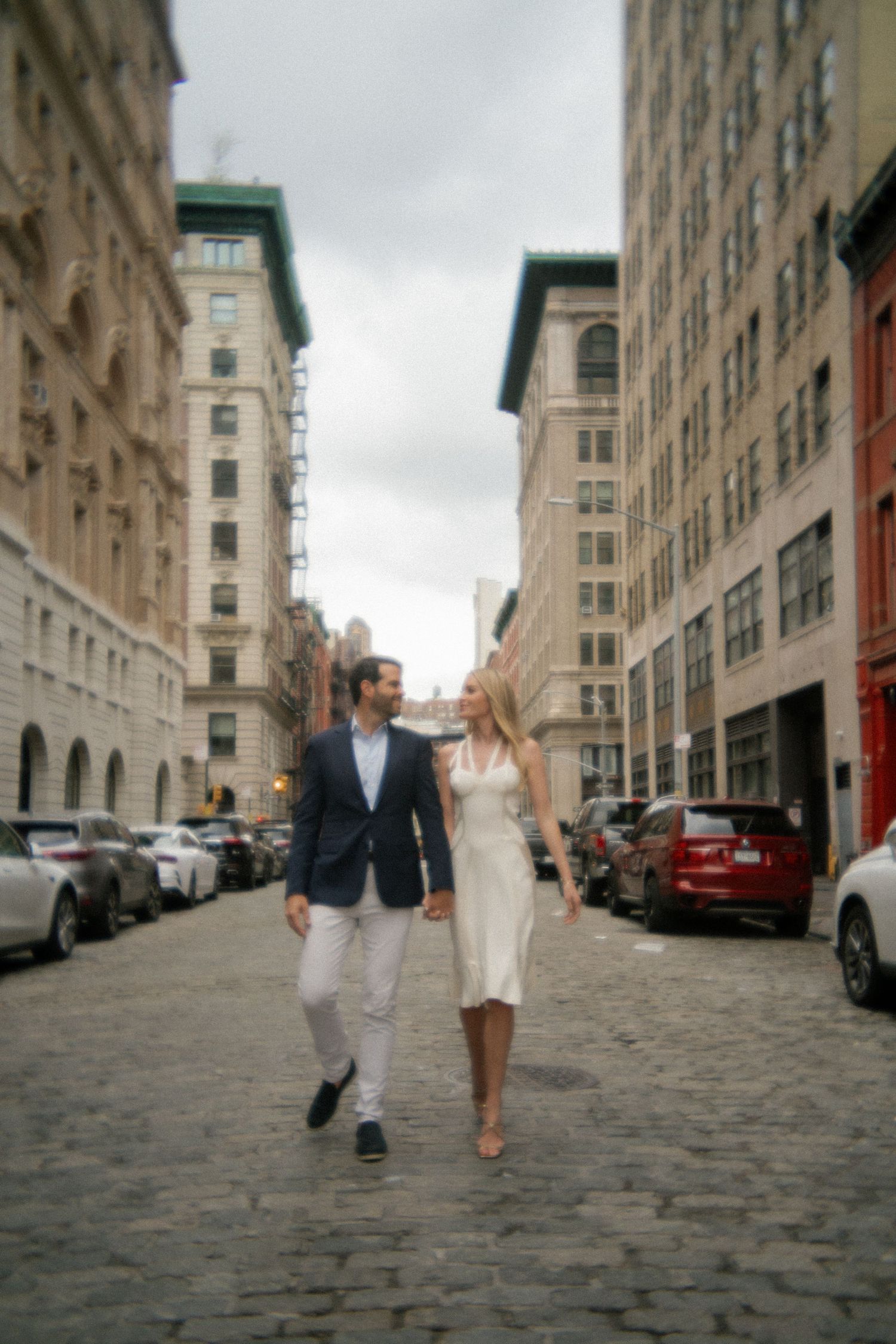 Wide angle view of couple walking on cobblestone street with historic buildings and cloudy sky.