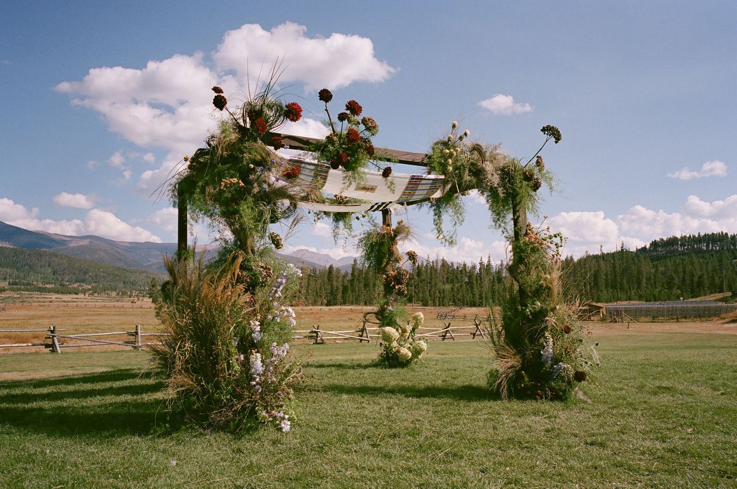Rustic outdoor wedding ceremony setup with wooden benches and mountain views in the background.