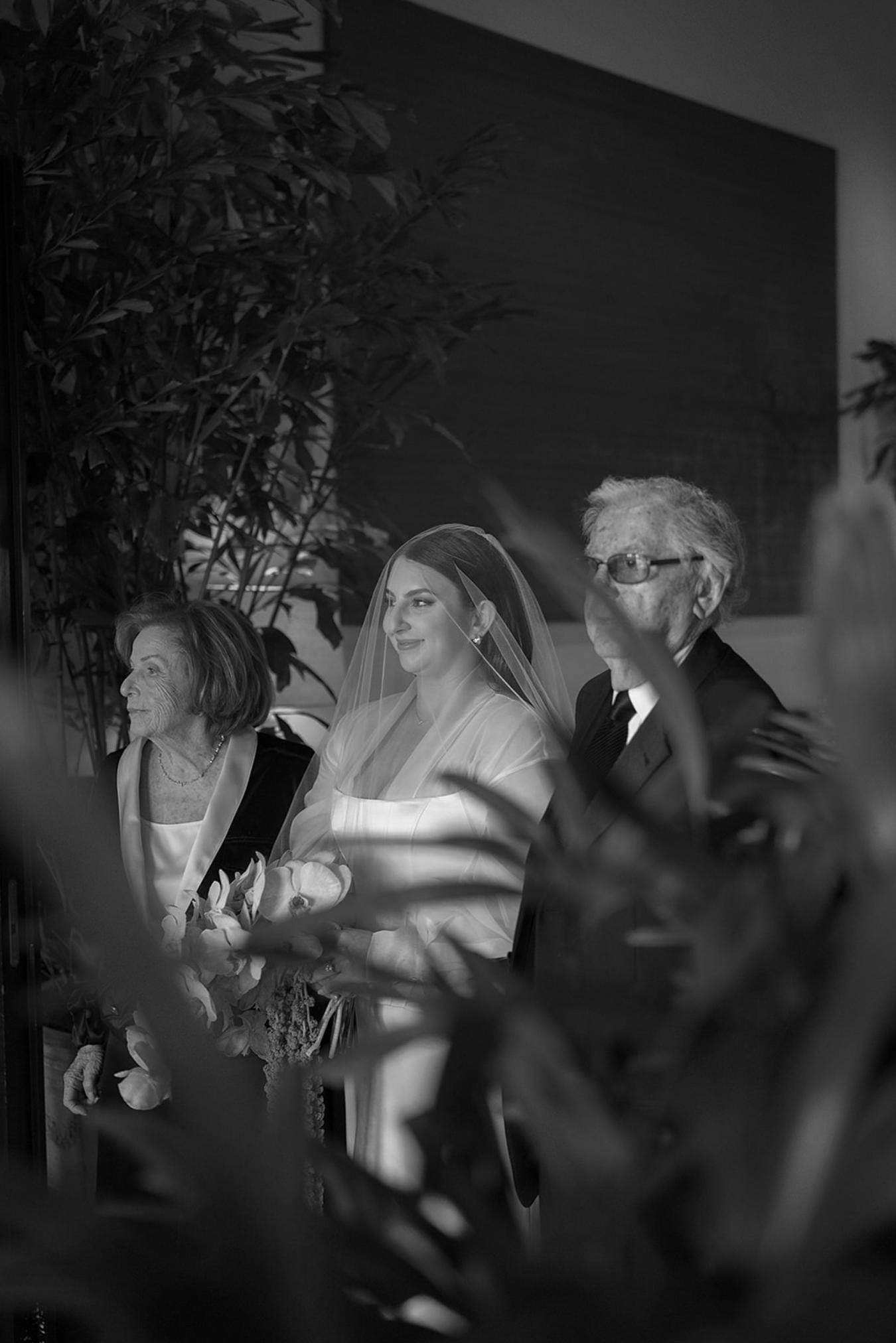 Black and white candid moment captured during a wedding ceremony through foliage.