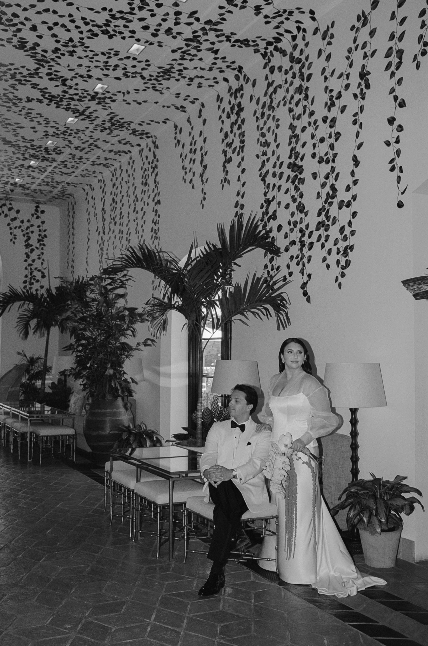 Black and white photo of a formal event with hanging vine decorations and palm trees.