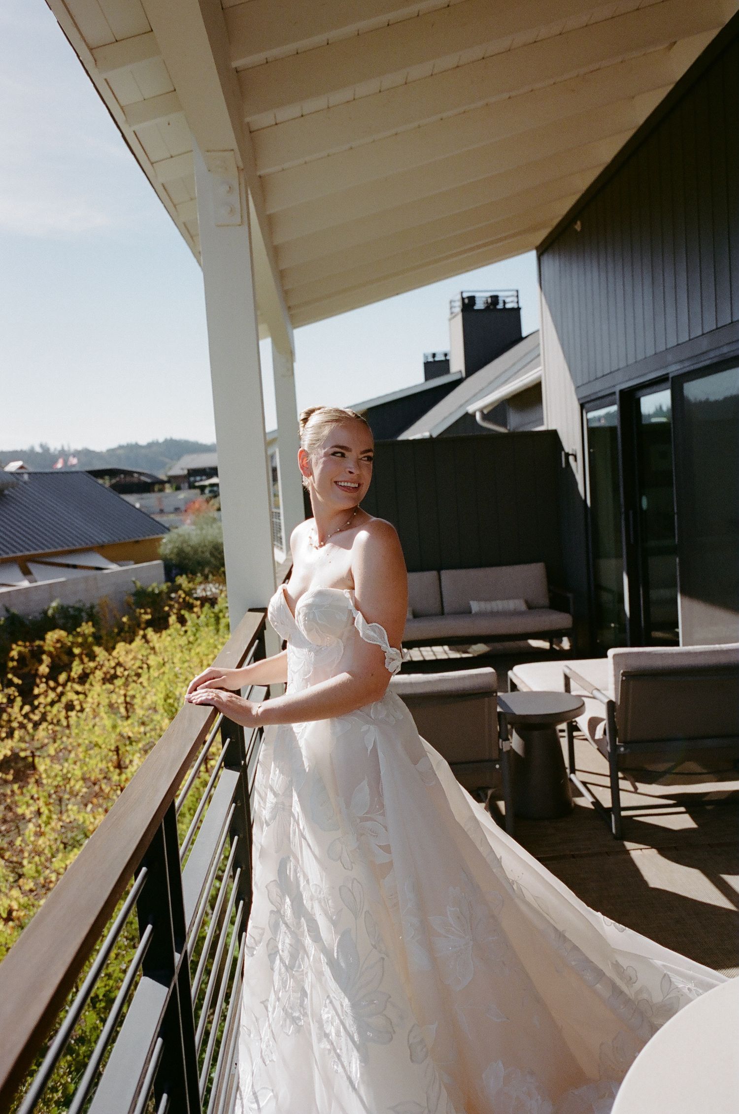 A bride in white gown standing on a balcony overlooking mountains.