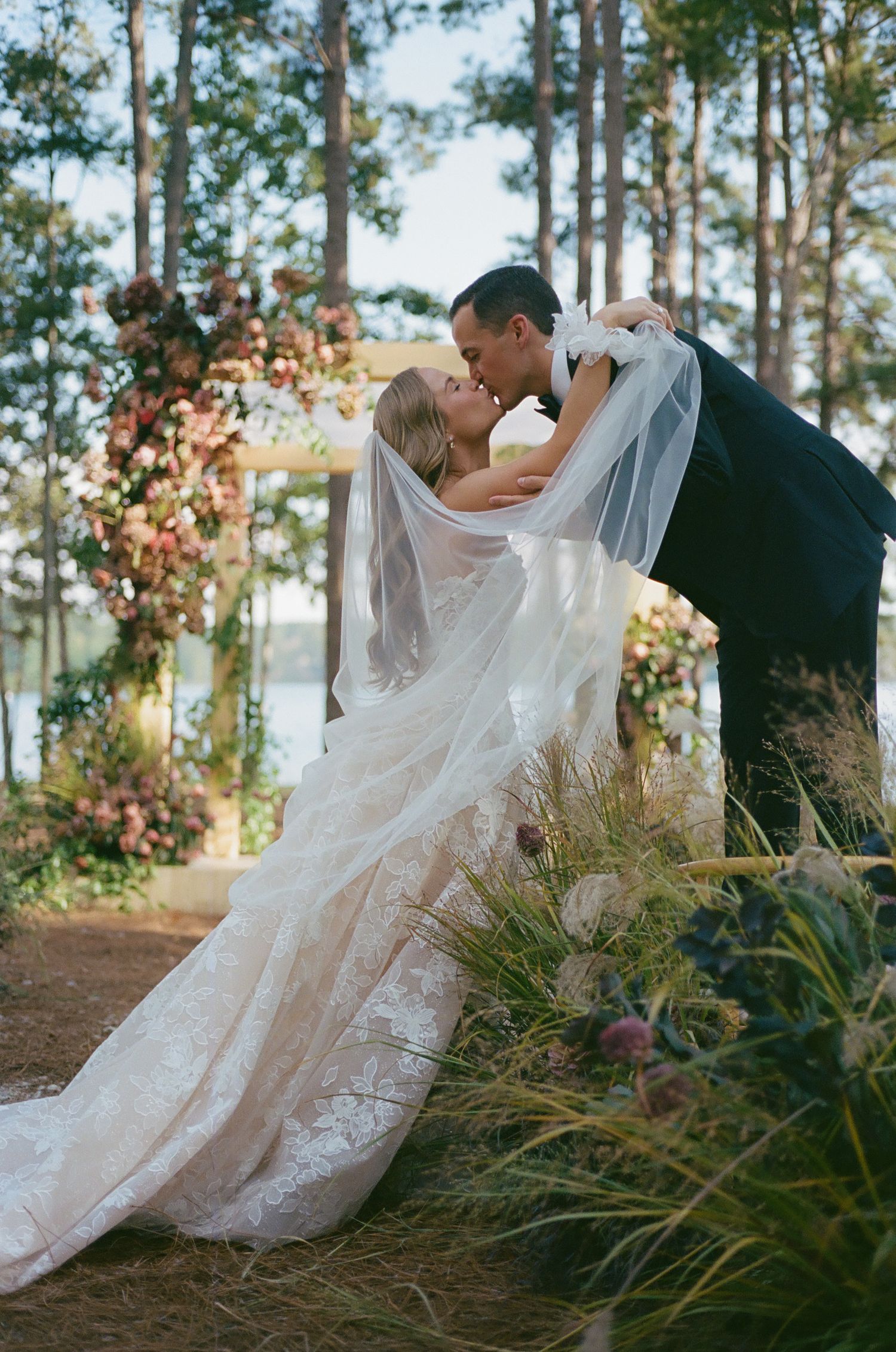 Romantic outdoor wedding portraits among tall pine trees with flowing lace dress details.