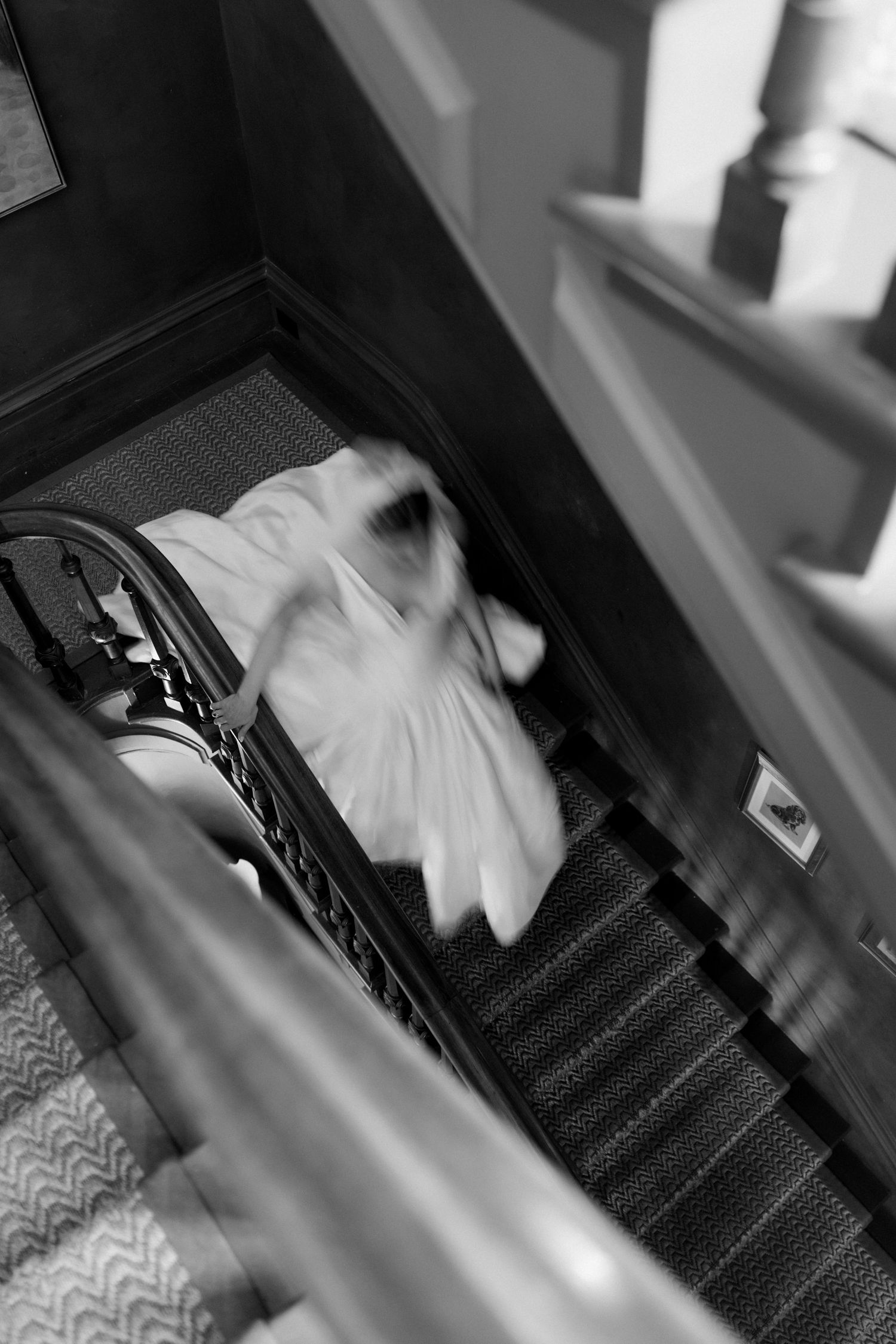 Blurred black and white photo of a bride in white dress descending an elegant staircase with iron railings.