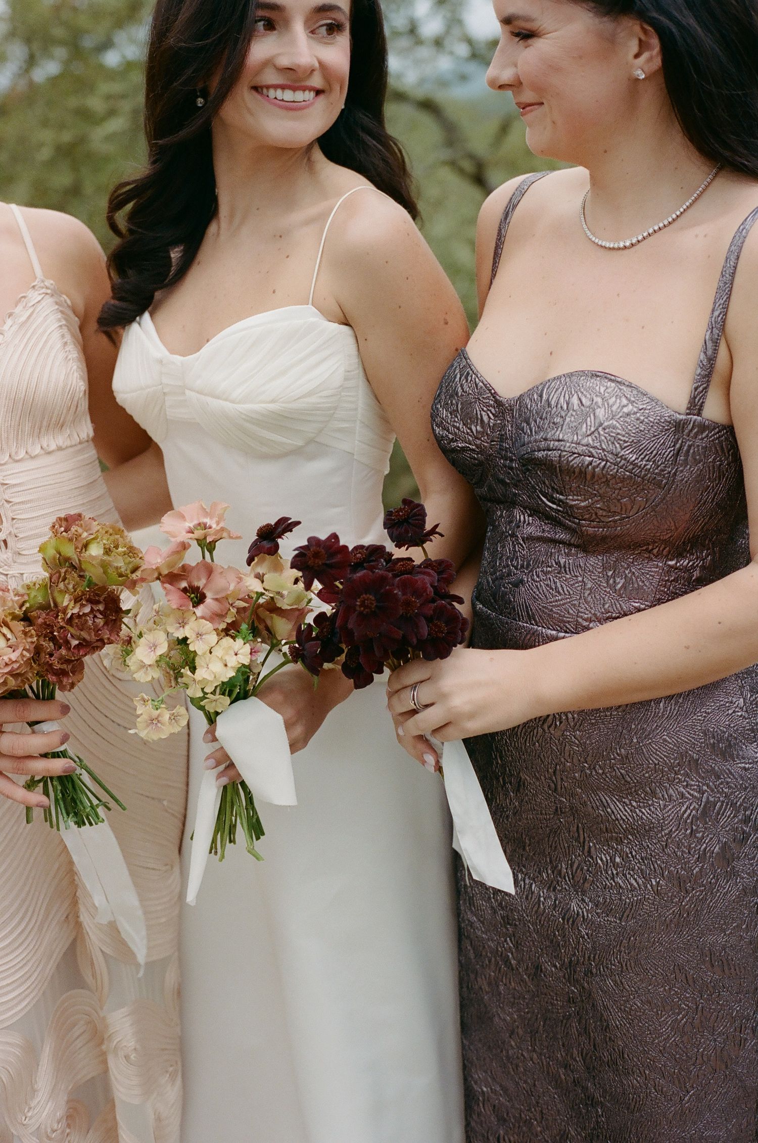 Bridesmaids in elegant metallic dresses hold romantic burgundy and cream floral bouquets.