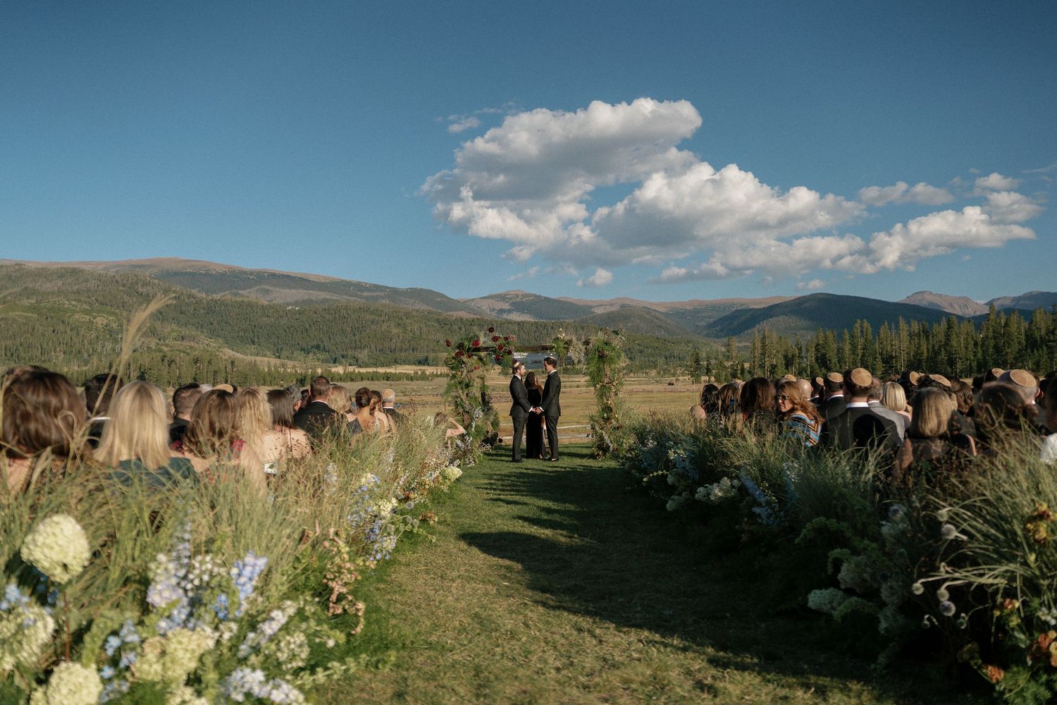 Mountain wedding ceremony site with guests gathered under blue skies.