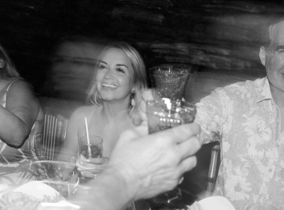 Black and white photo of a festive wedding reception celebration with guests enjoying drinks and dancing.