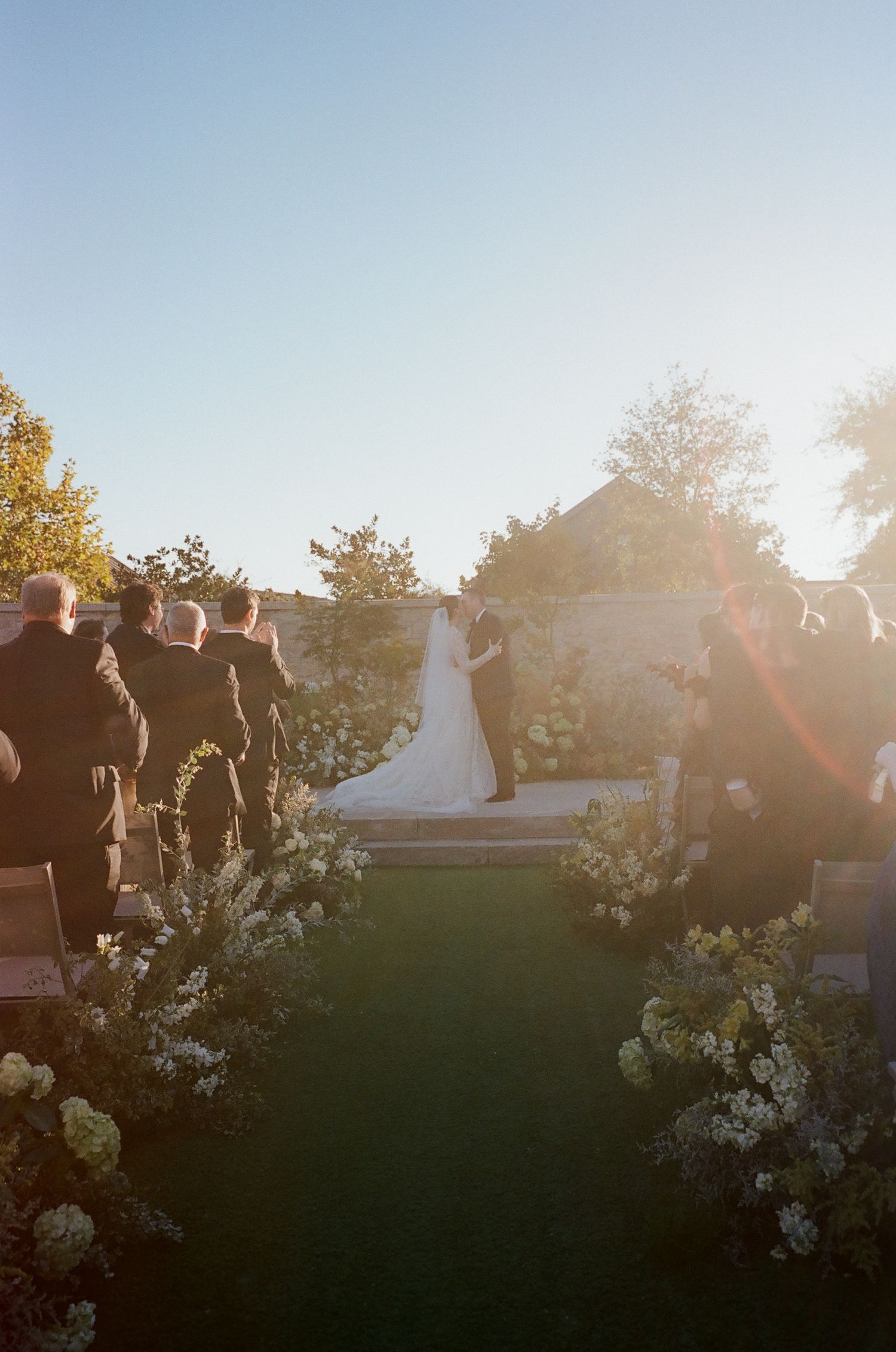 Wedding ceremony setup outdoors with white floral arrangements and natural sunlight.
