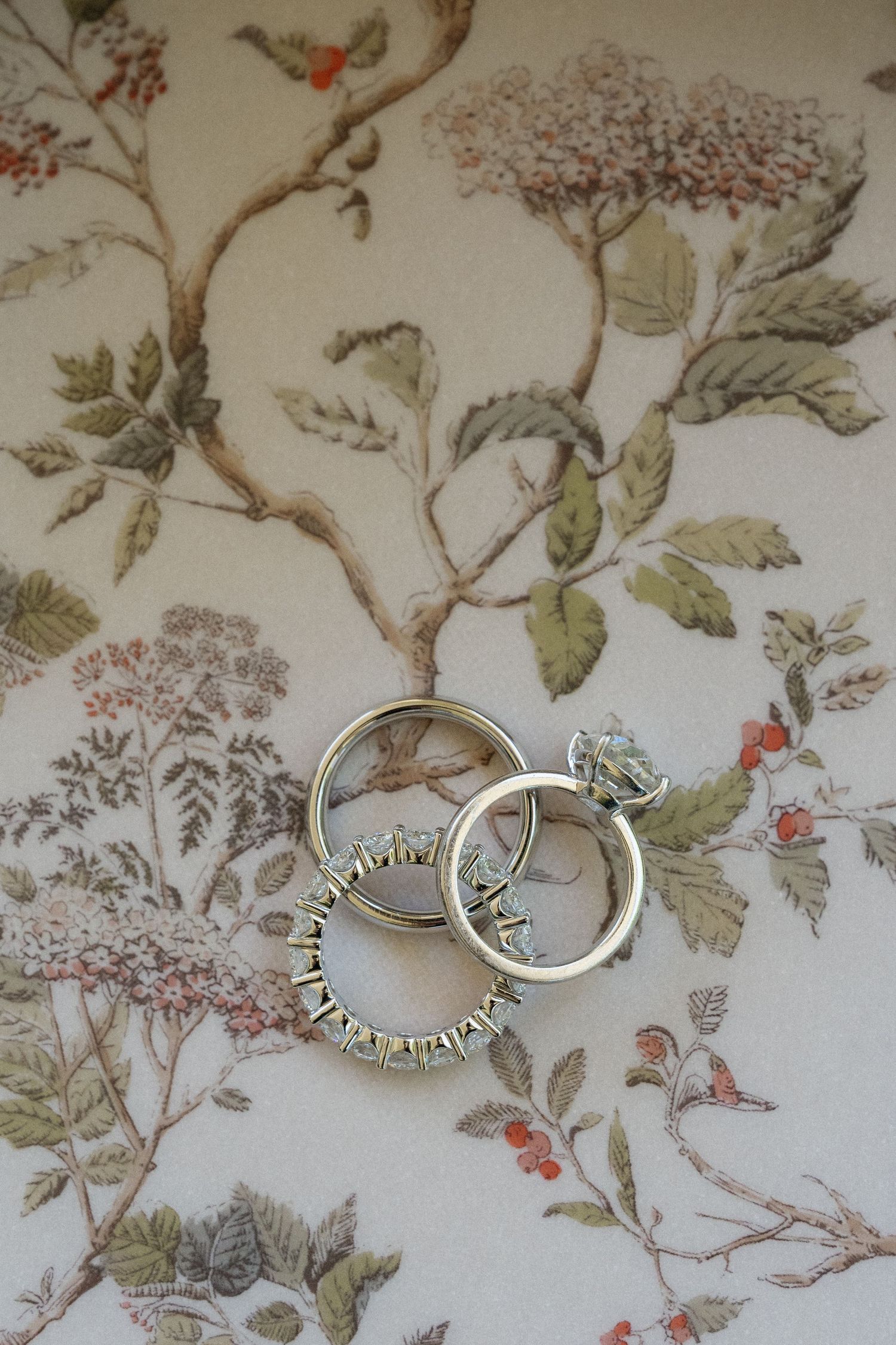 Three elegant wedding rings displayed on a floral botanical background.