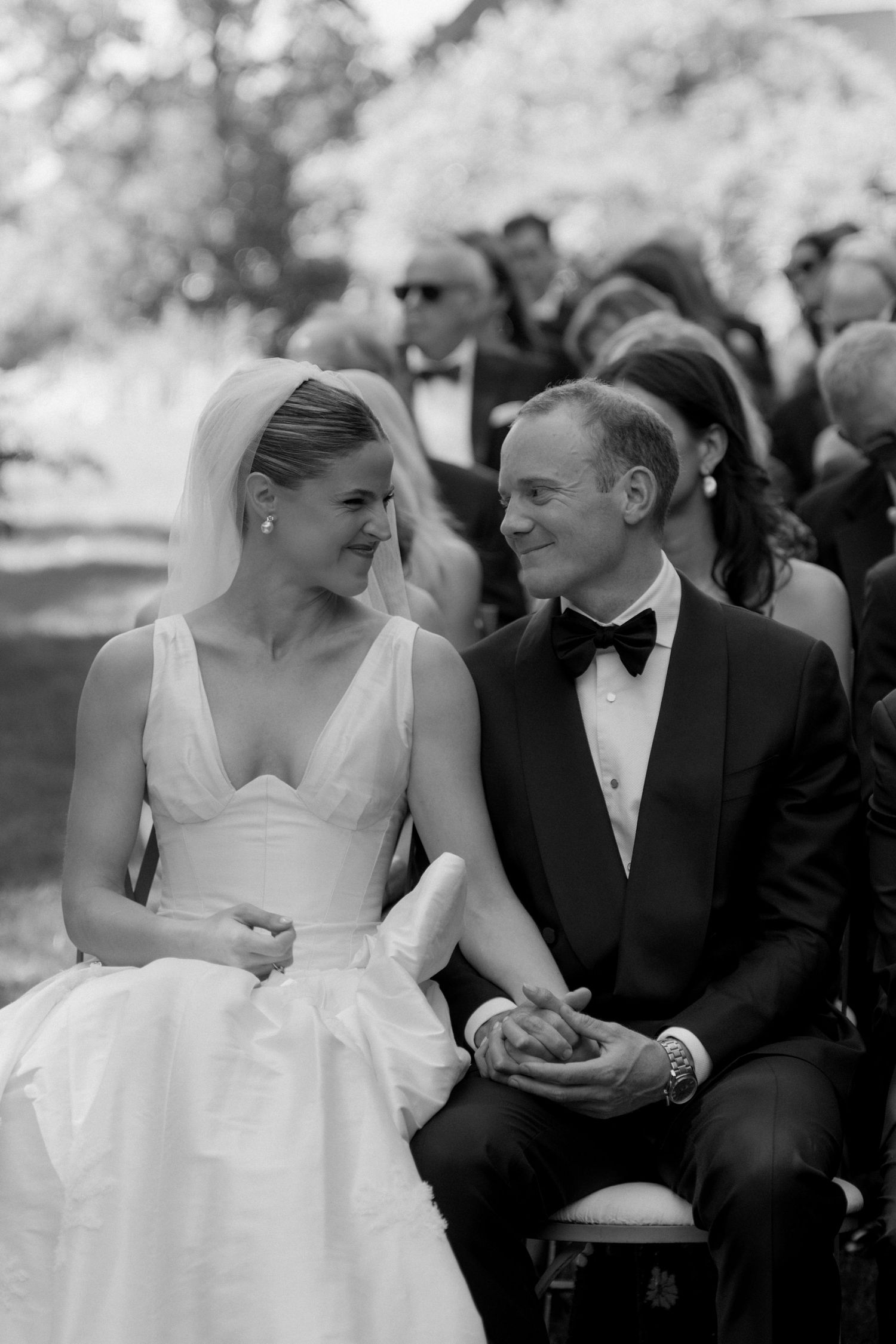 Black and white photo of a smiling bride and groom holding hands during their outdoor wedding ceremony.