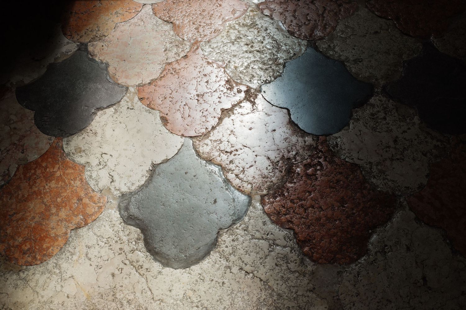 Vintage decorative floor tiles in scalloped shapes with weathered stone texture in gray, red, and beige tones.