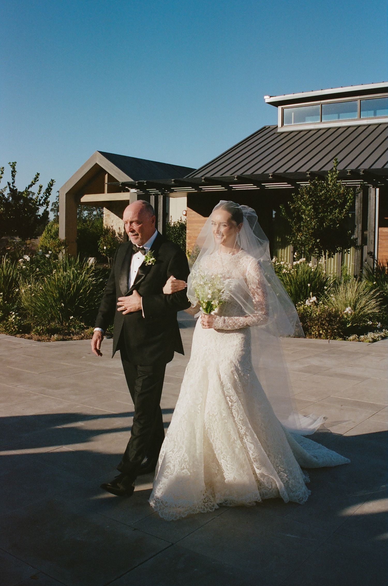 A wedding couple posing for photos outside a modern building on their special day.
