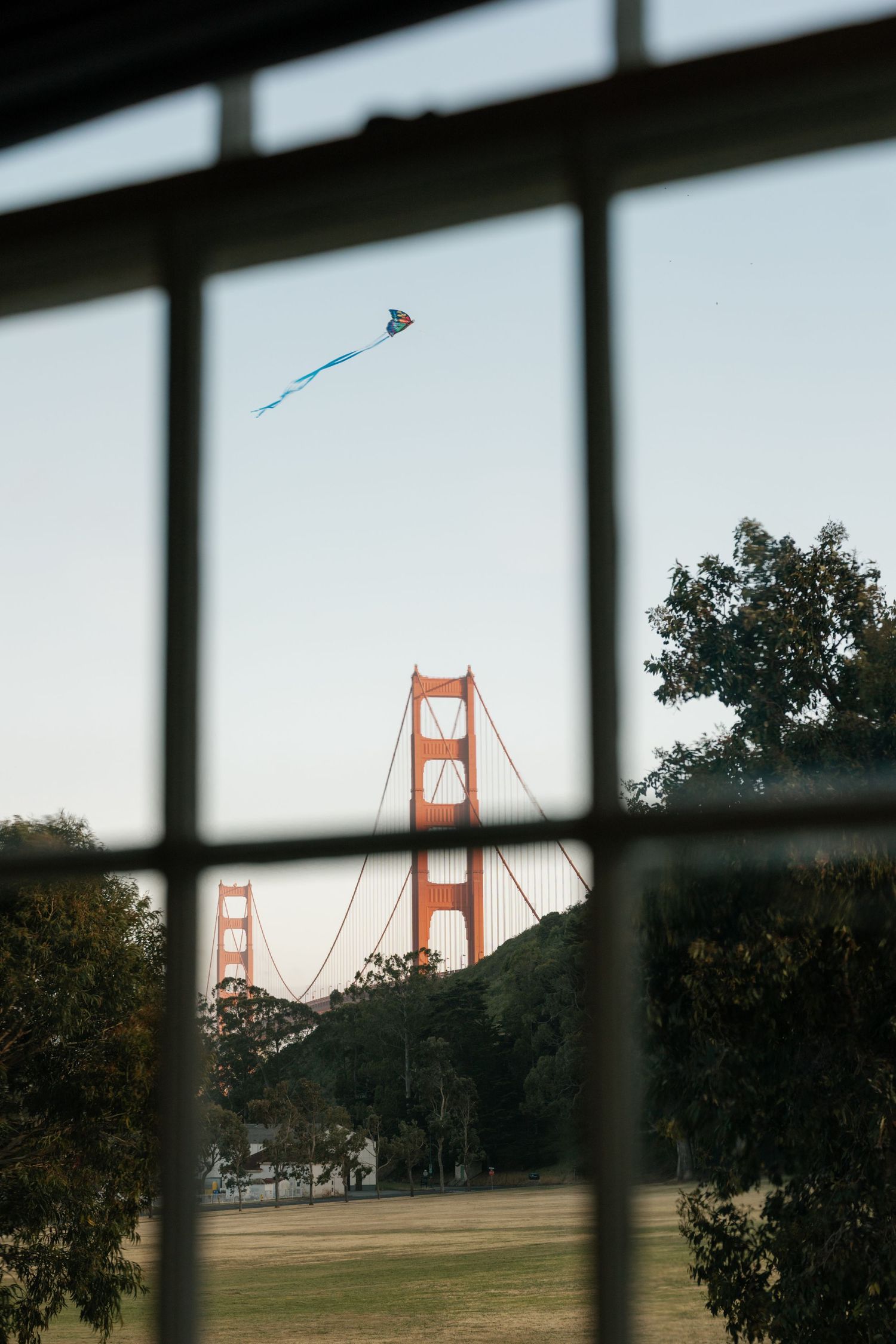 View of the Golden Gate Bridge through a window frame with a blue kite flying in the sky.