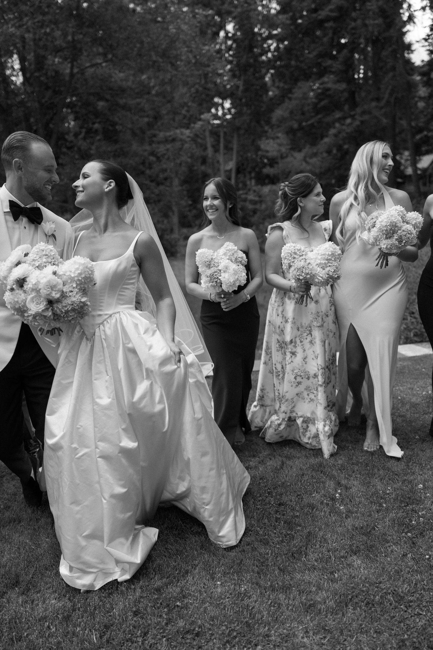 Black and white photo of wedding party walking with flowing dresses and bouquets.