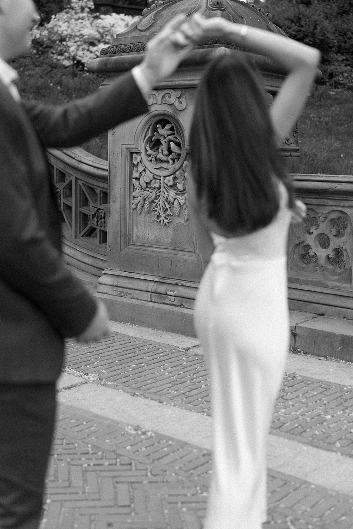 Elegant couple dancing outdoors near decorative stone wall in black and white sequence.