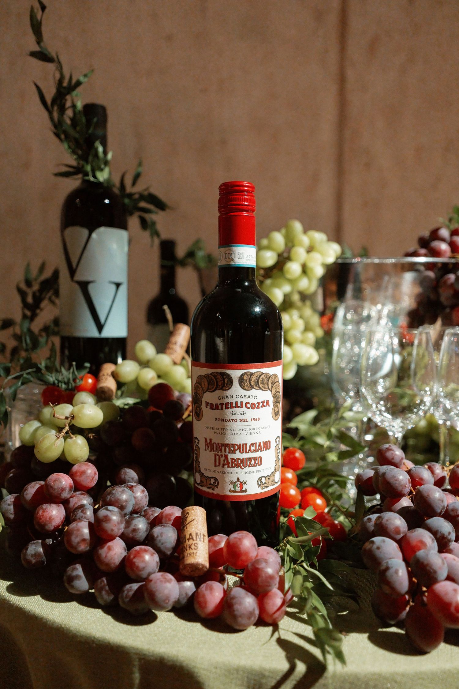 A still life image featuring a bottle of red wine surrounded by grapes and wine glasses.