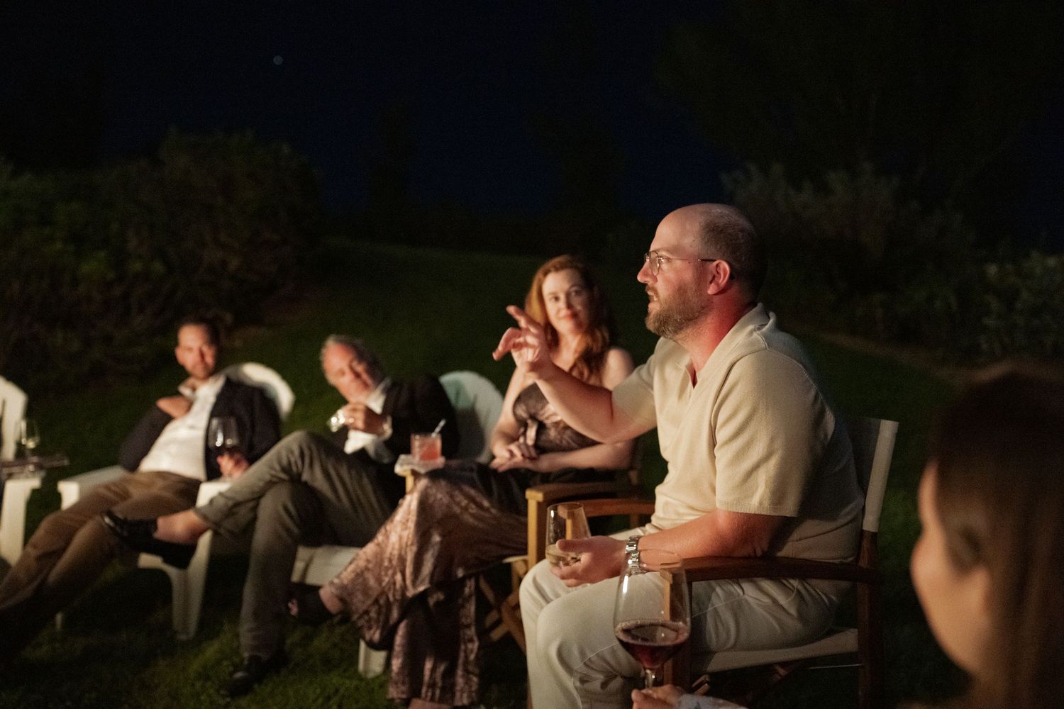 A group of people sitting around a fire pit and talking at night in an outdoor setting.