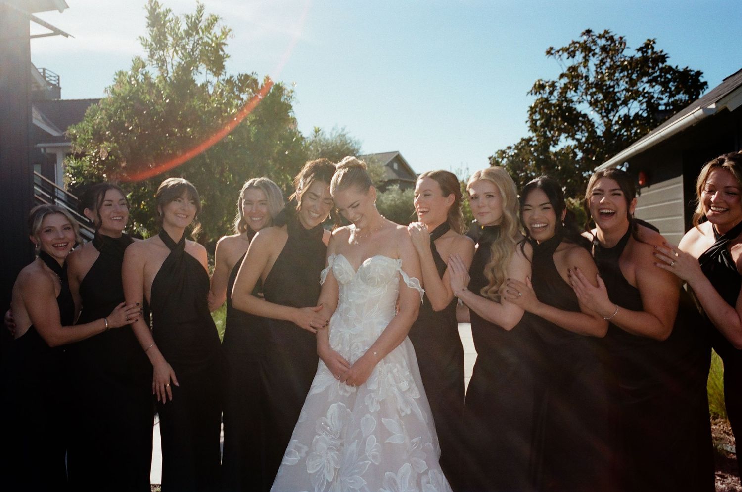 Wedding party in black dresses posing outdoors at sunset.