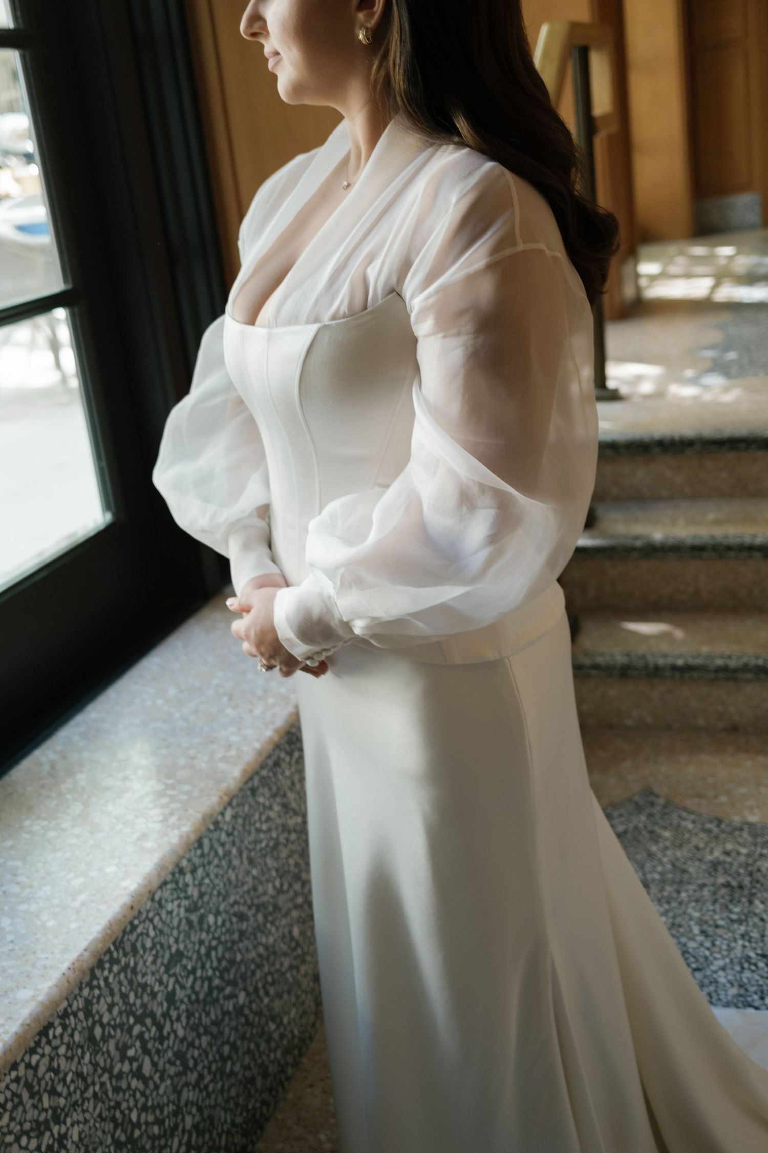 A side view of an elegant white wedding dress with dramatic sheer puff sleeves near a window.
