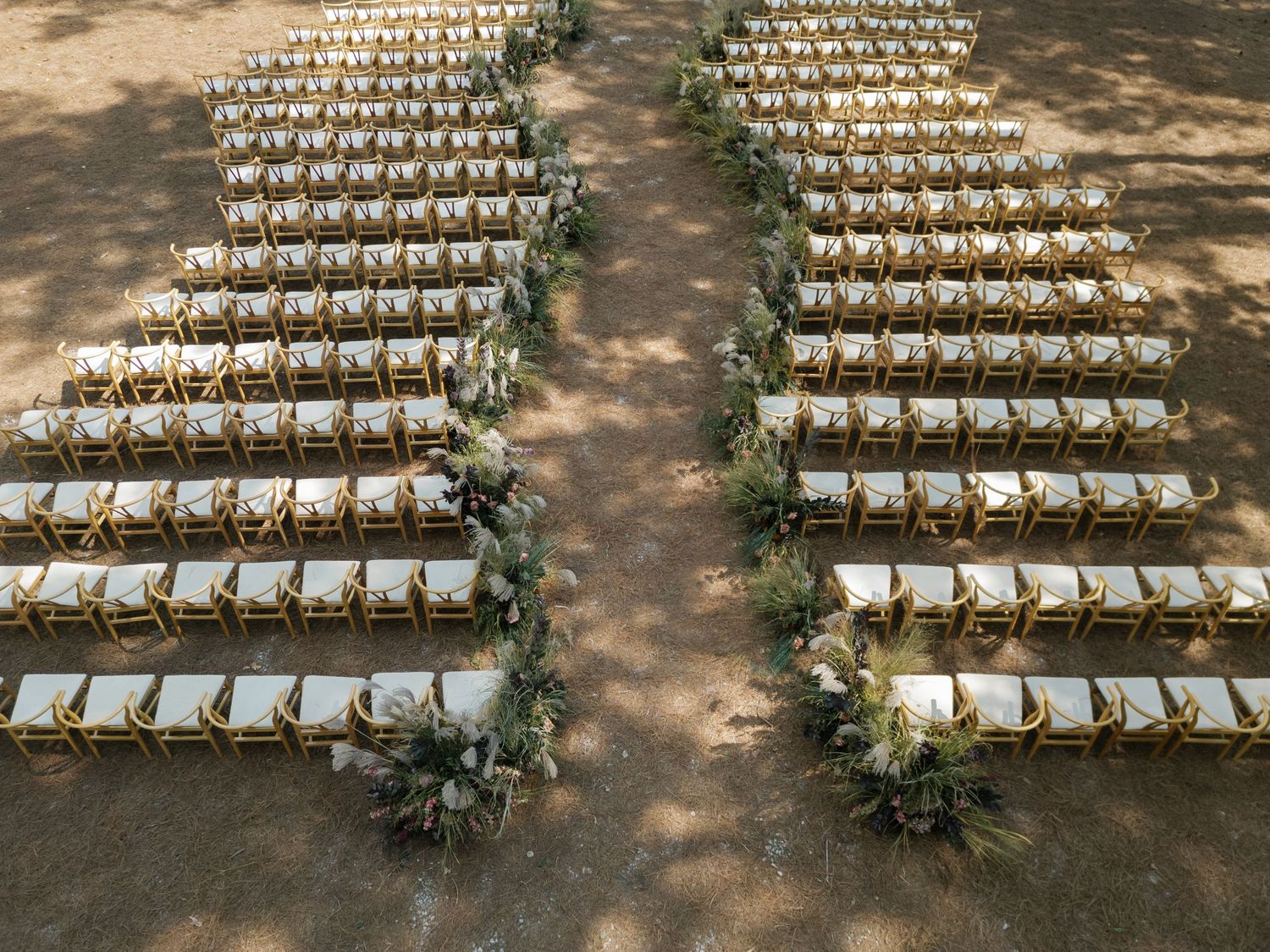 Outdoor wedding ceremony setup with white chairs arranged in rows under dappled sunlight.