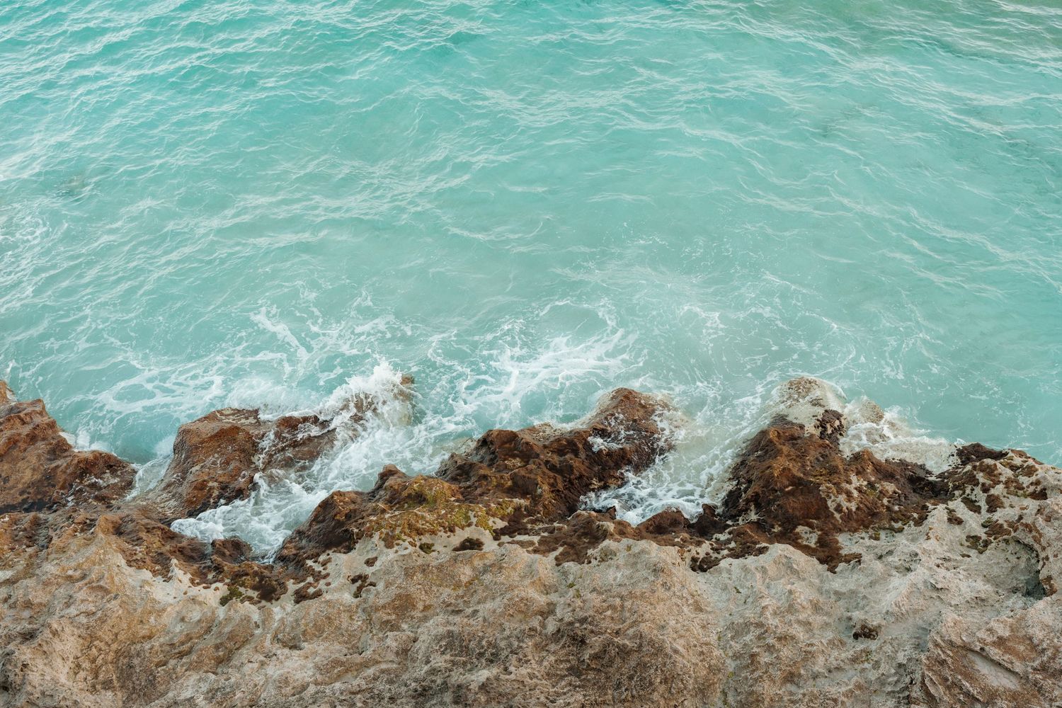 Tranquil turquoise waters crash against rugged rocky coastline in this serene natural landscape.