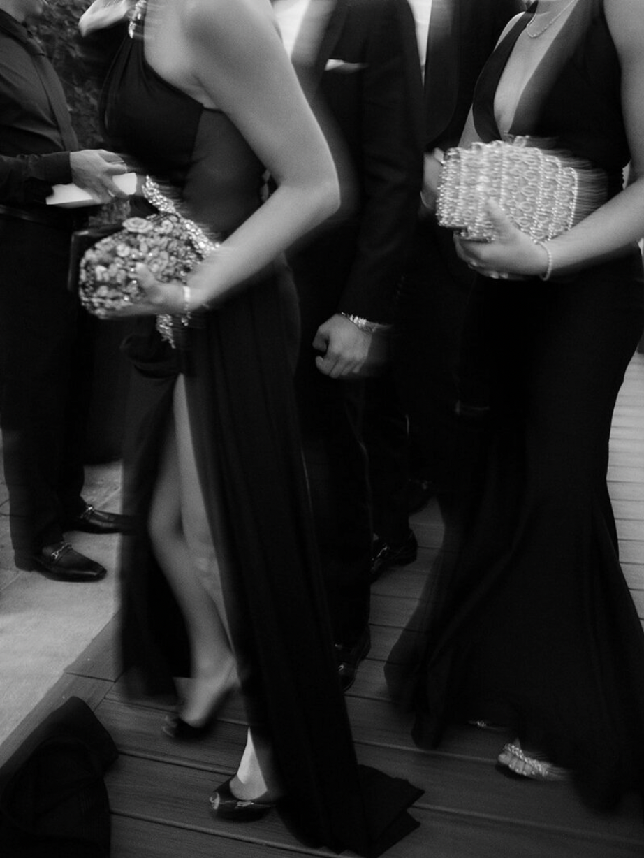 Black and white photo of formal wedding guests holding clutch purses at an elegant reception.