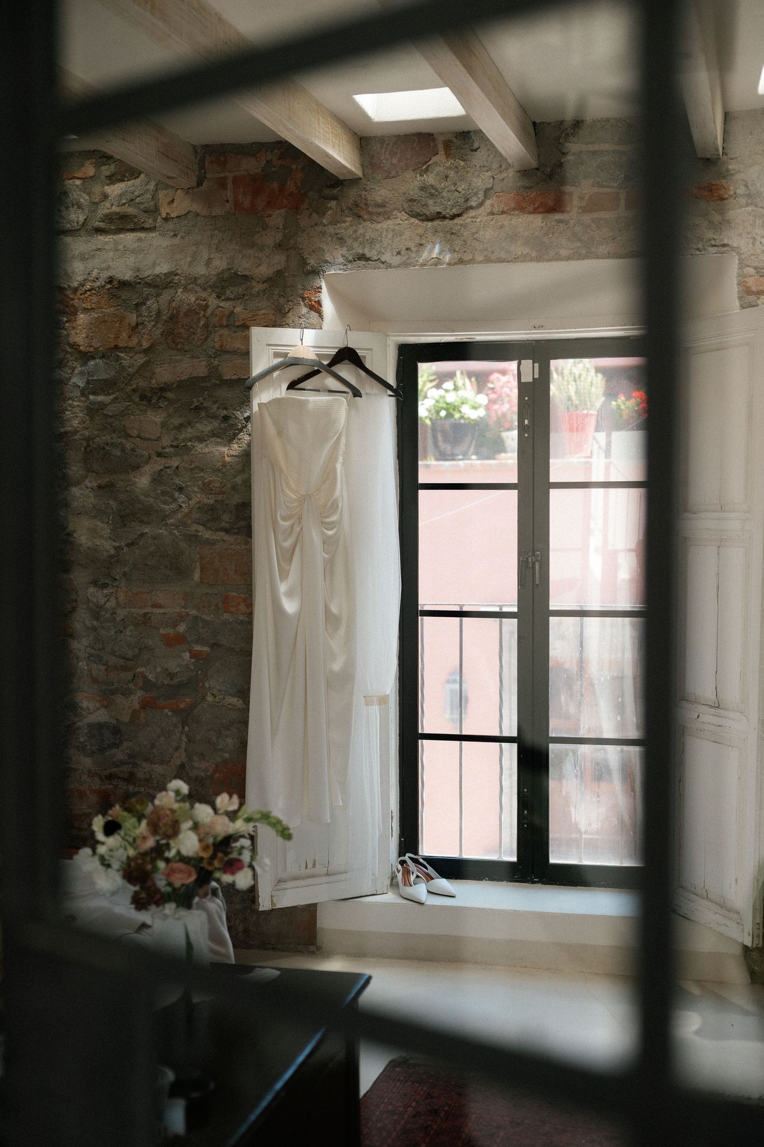Sunlit room with exposed brick walls, white curtains, and wedding dresses hanging by windows.