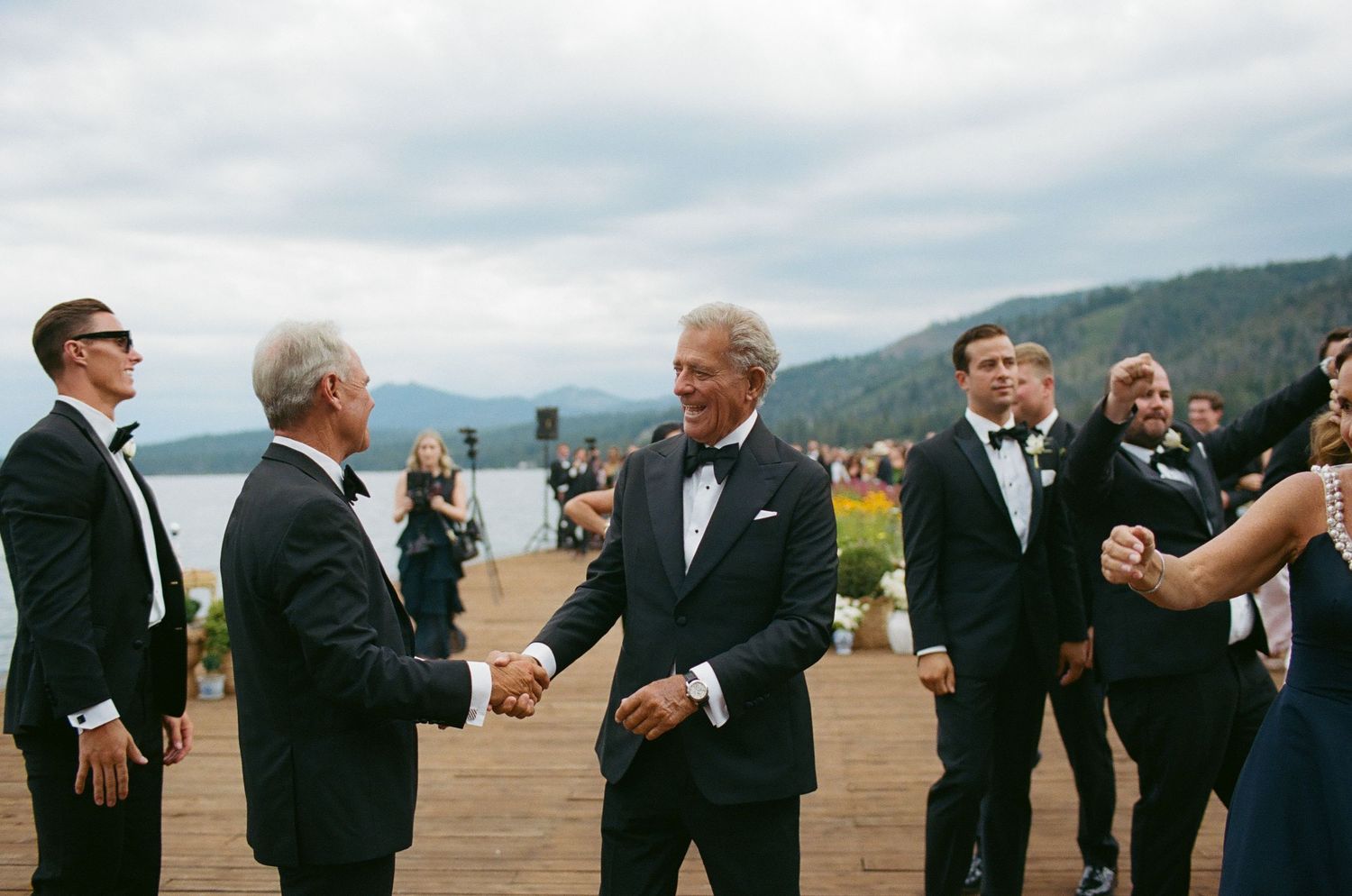 Groomsmen in black tuxedos line up against a scenic mountain backdrop.