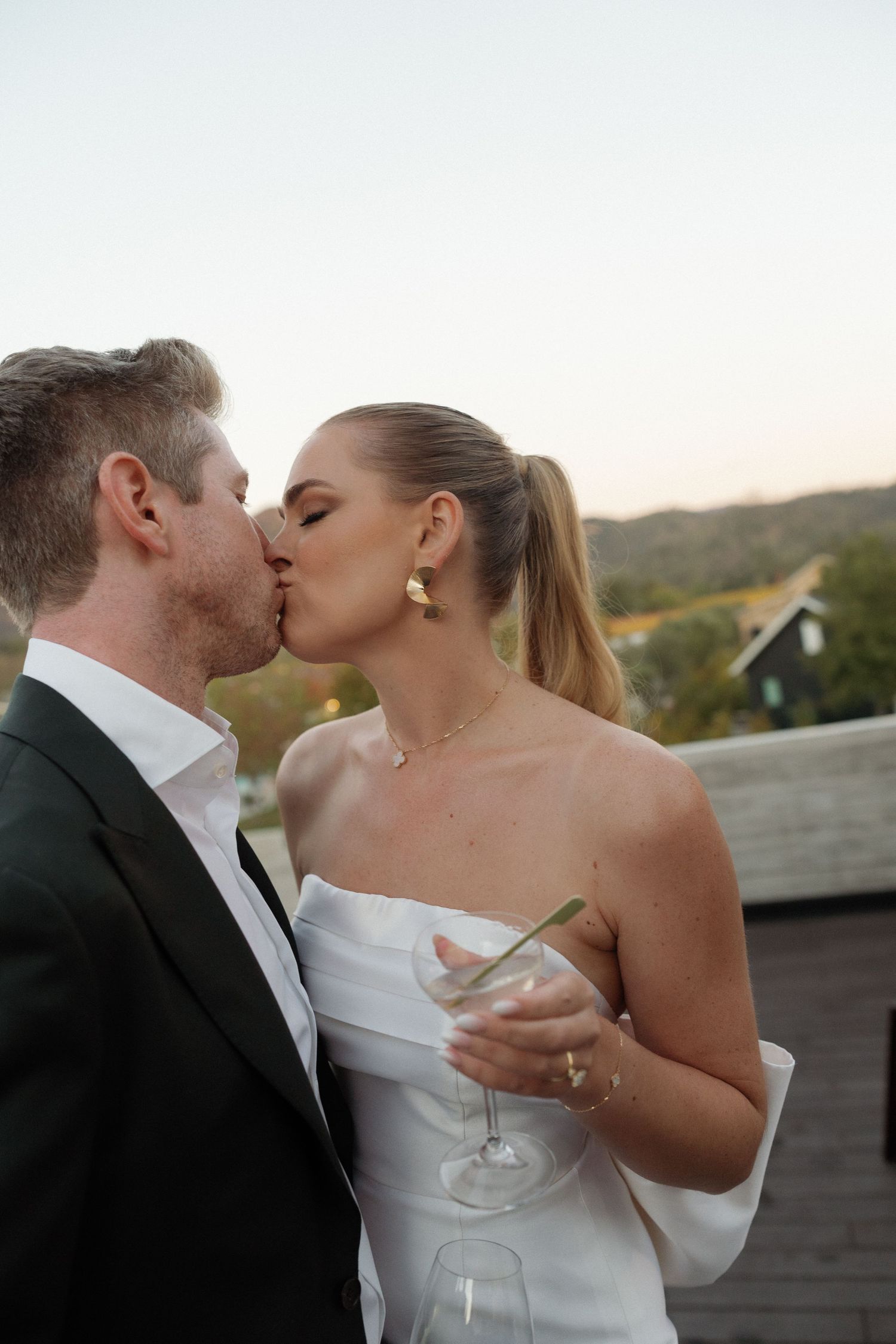 Romantic wedding moment captured at sunset with a white bridal gown against a mountain backdrop.