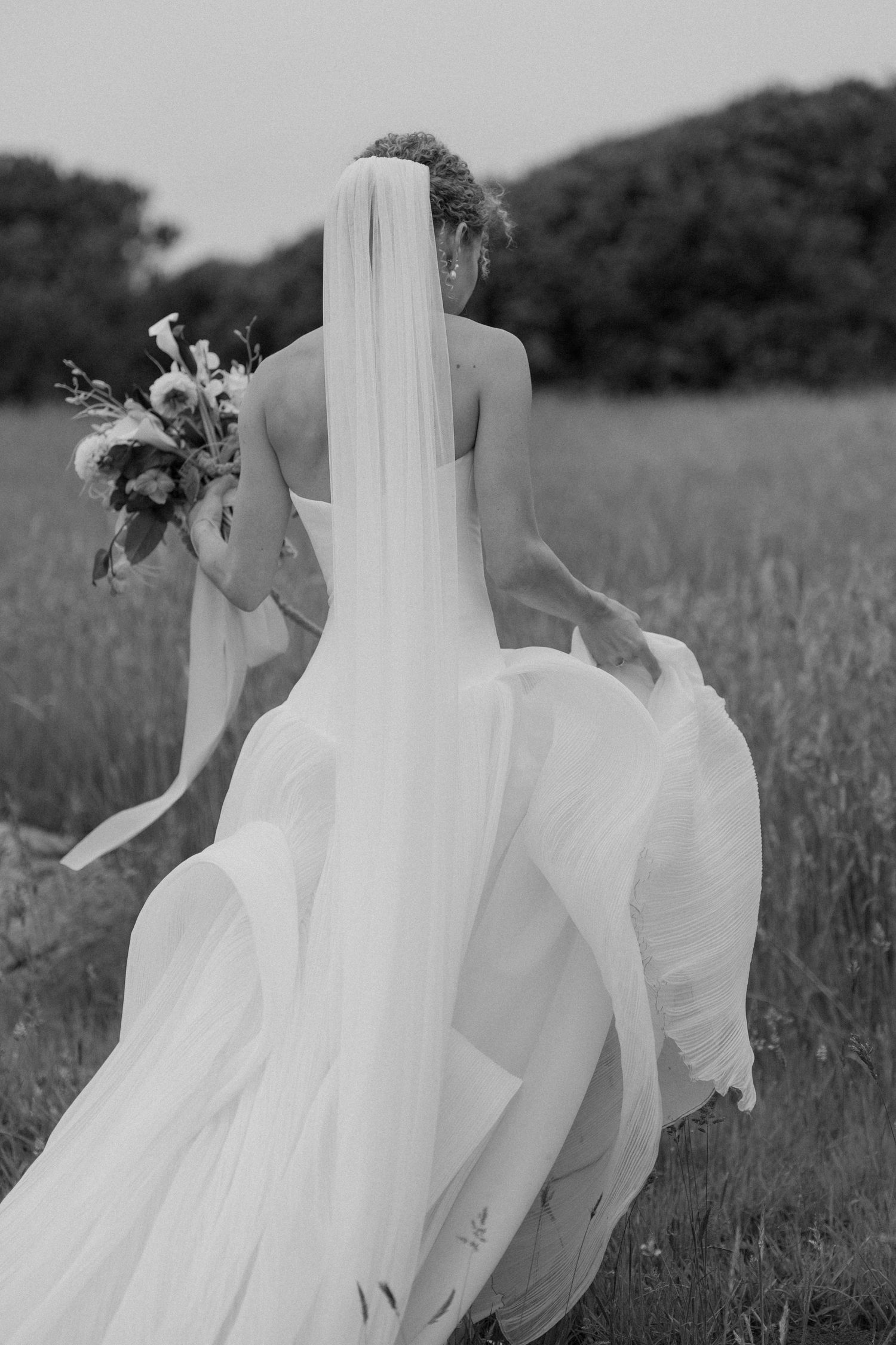 Bride's white dress flowing gracefully in field during outdoor photo session.