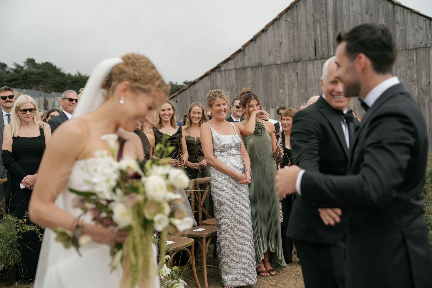 Wedding ceremony guests celebrate under cloudy skies at outdoor venue.