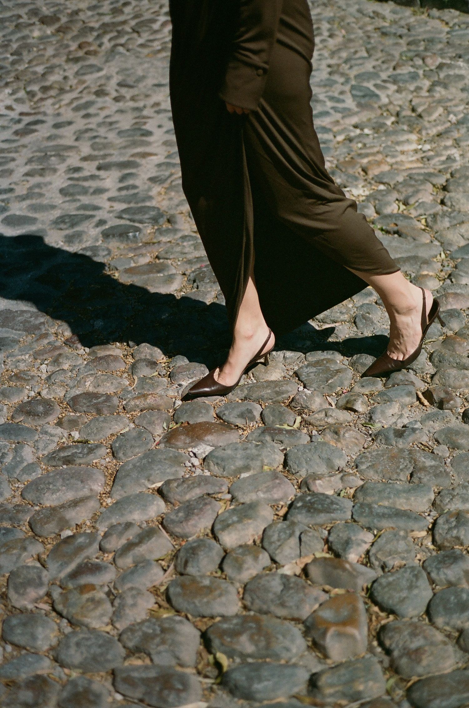 Bare feet walking on ancient cobblestone street in elegant flowing dress.