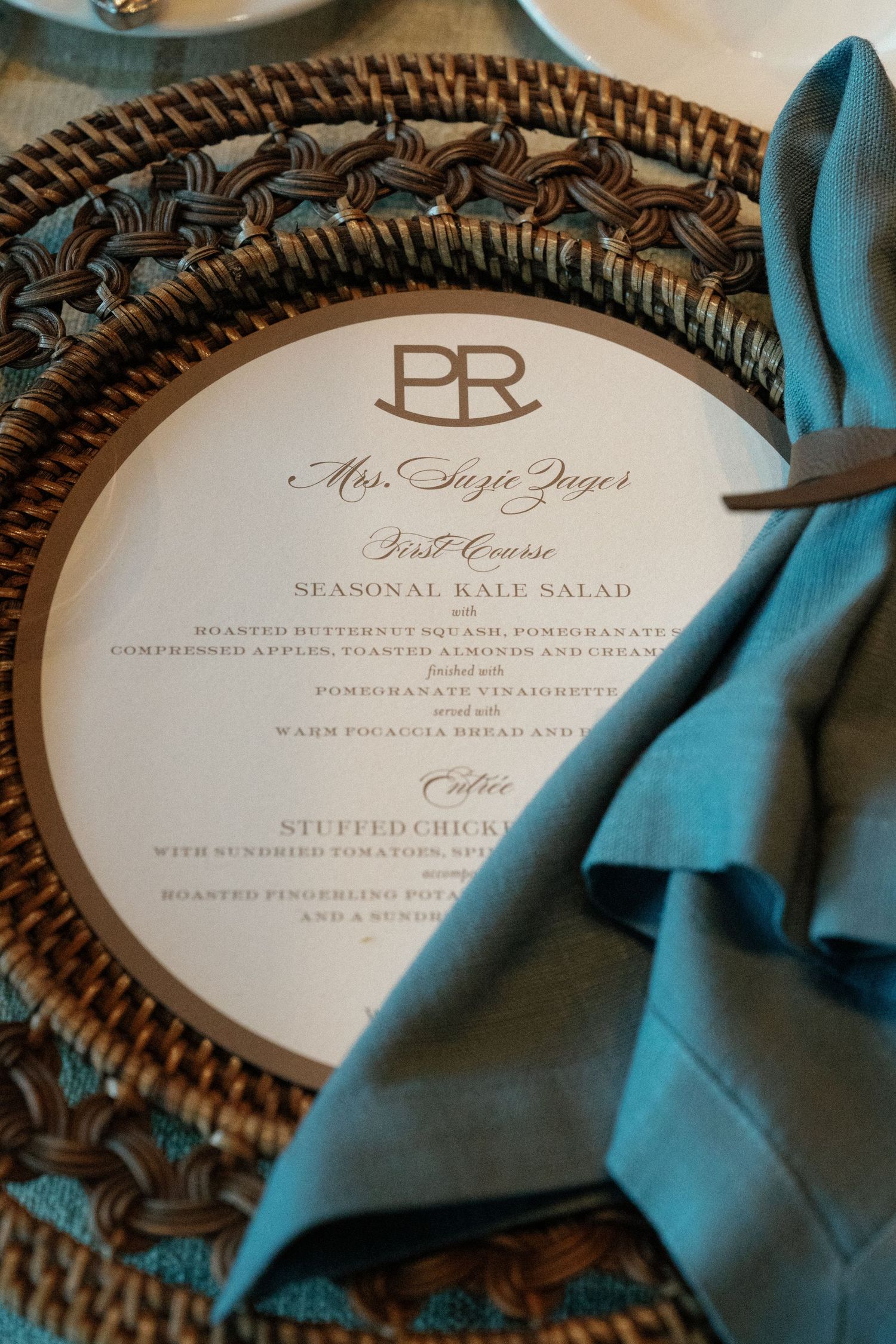 Wedding menu cards with elegant typography displayed on turquoise napkins and woven chargers.