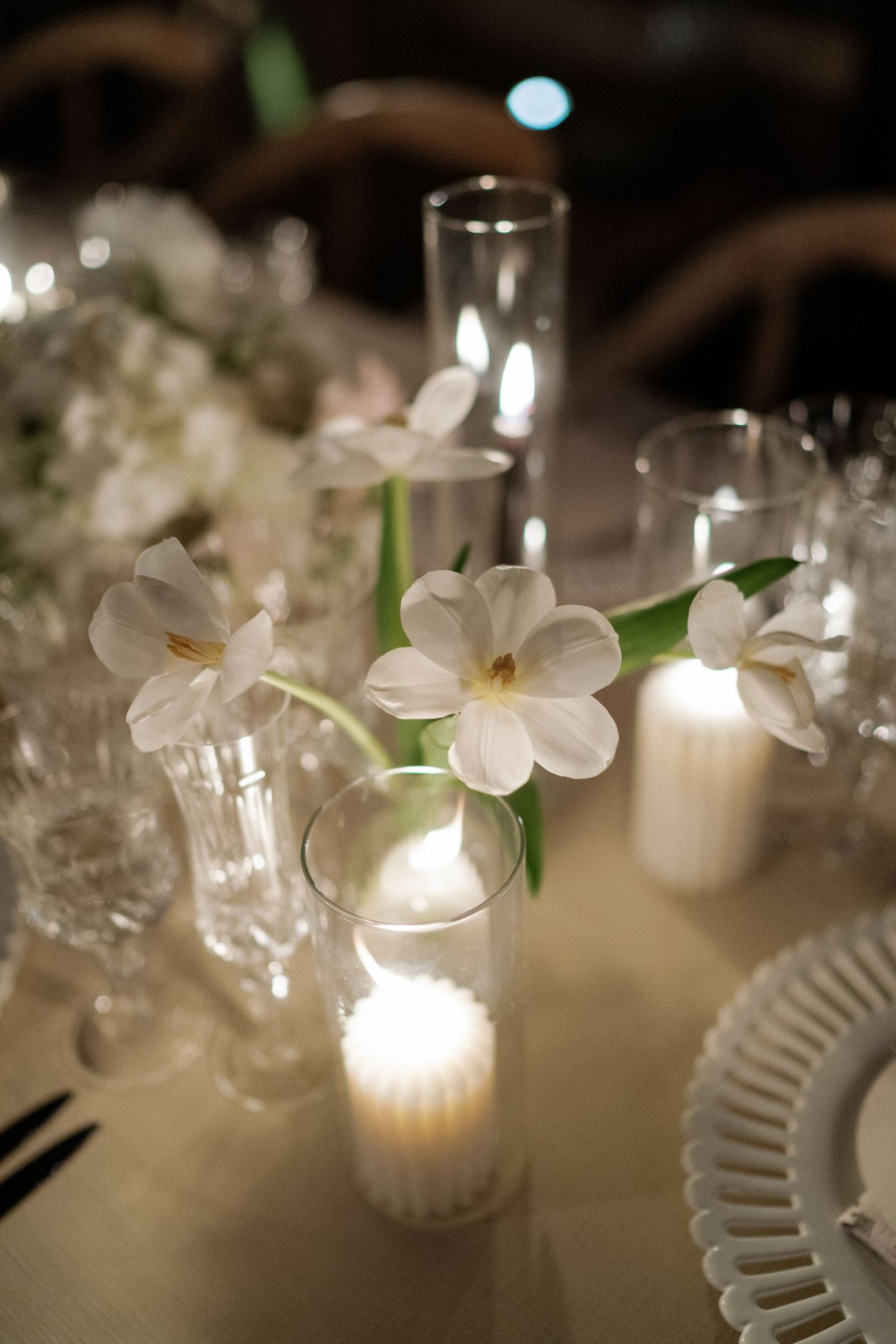 White floral centerpieces with glowing candles on elegant place settings.
