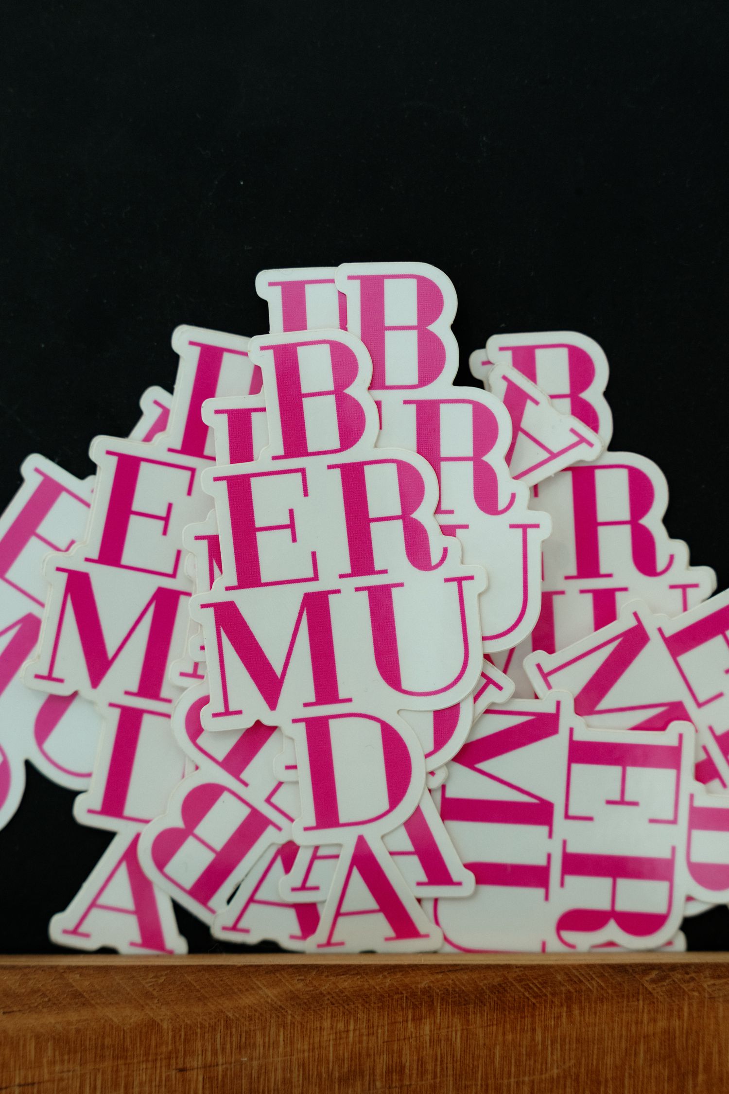 The image shows a collection of pink and white letter-shaped stickers on a dark background.