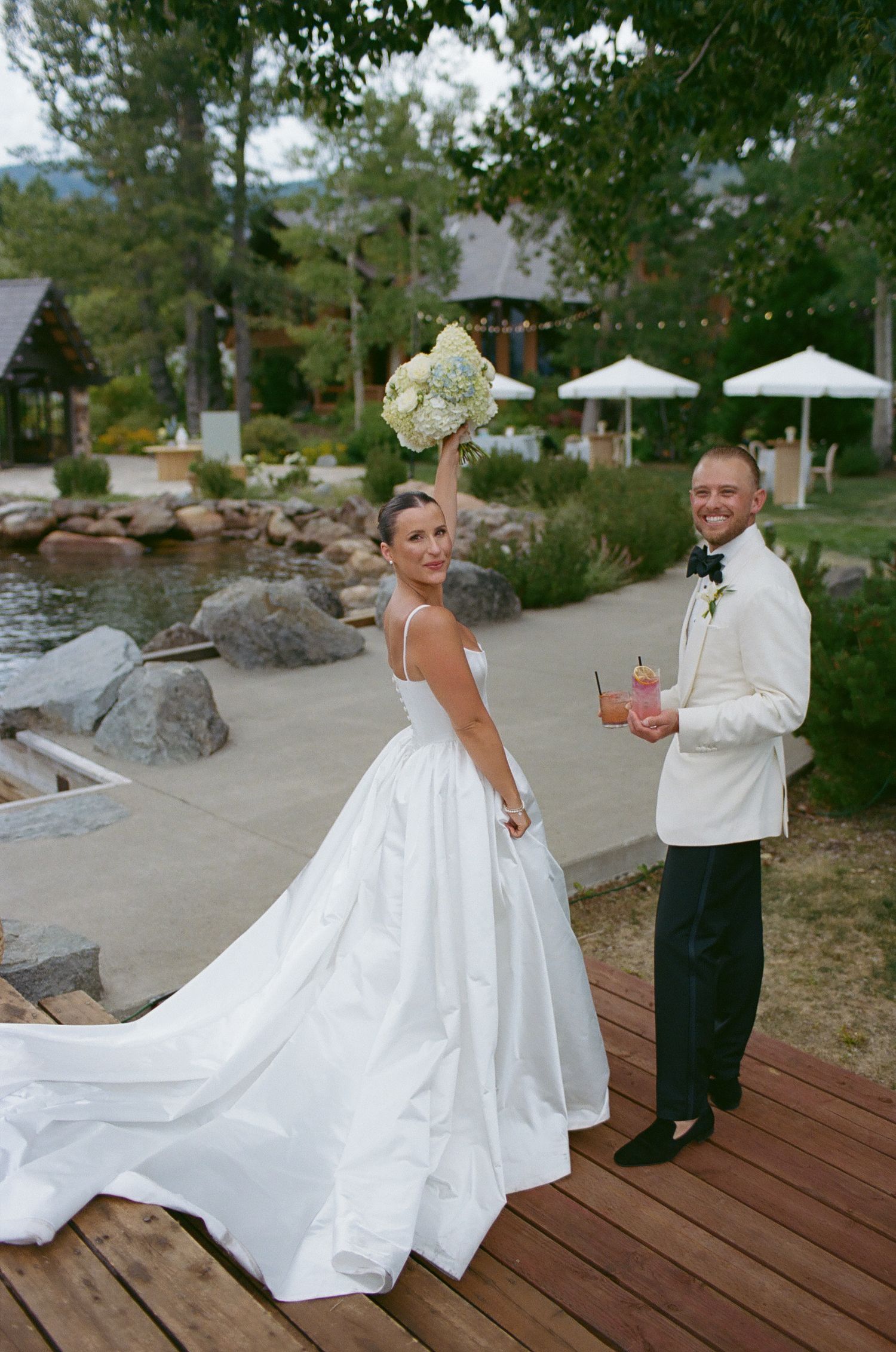 Newlyweds share playful moments on a wooden deck surrounded by natural scenery.