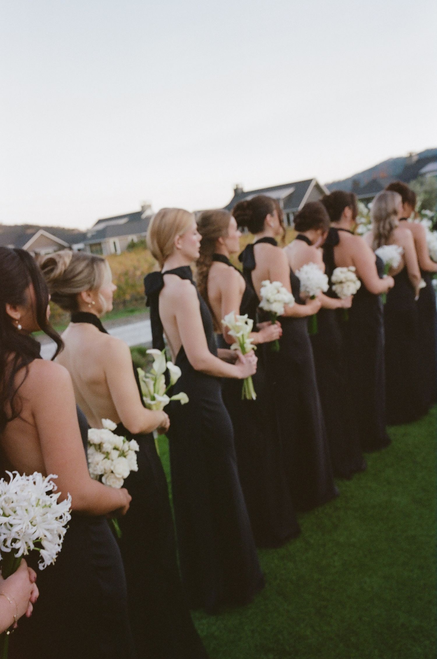 Line of attendants in navy and blush dresses holding white bouquets at an outdoor ceremony.