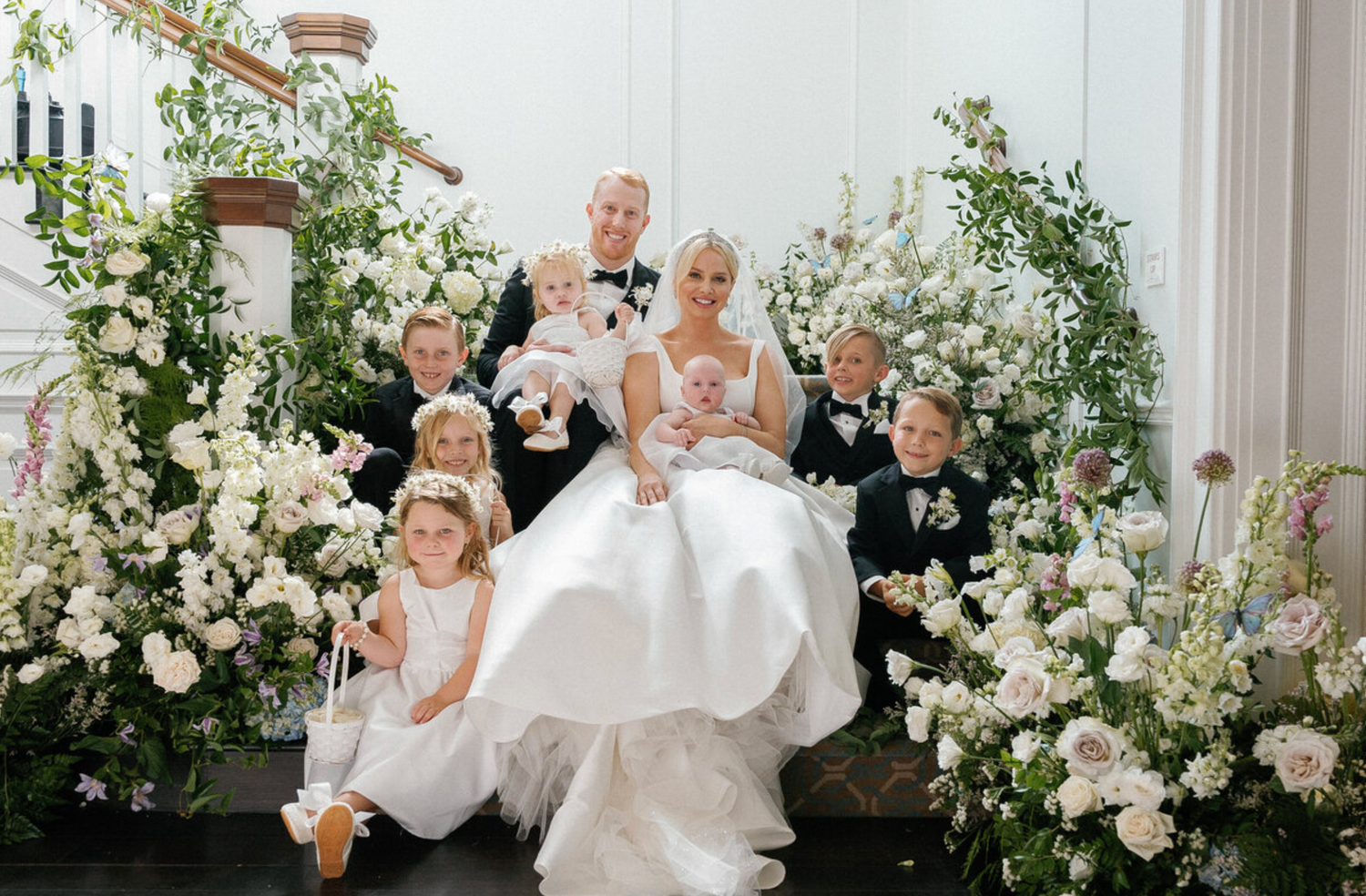 Wedding party portrait with floral arch decorations and elegant white and green arrangements.