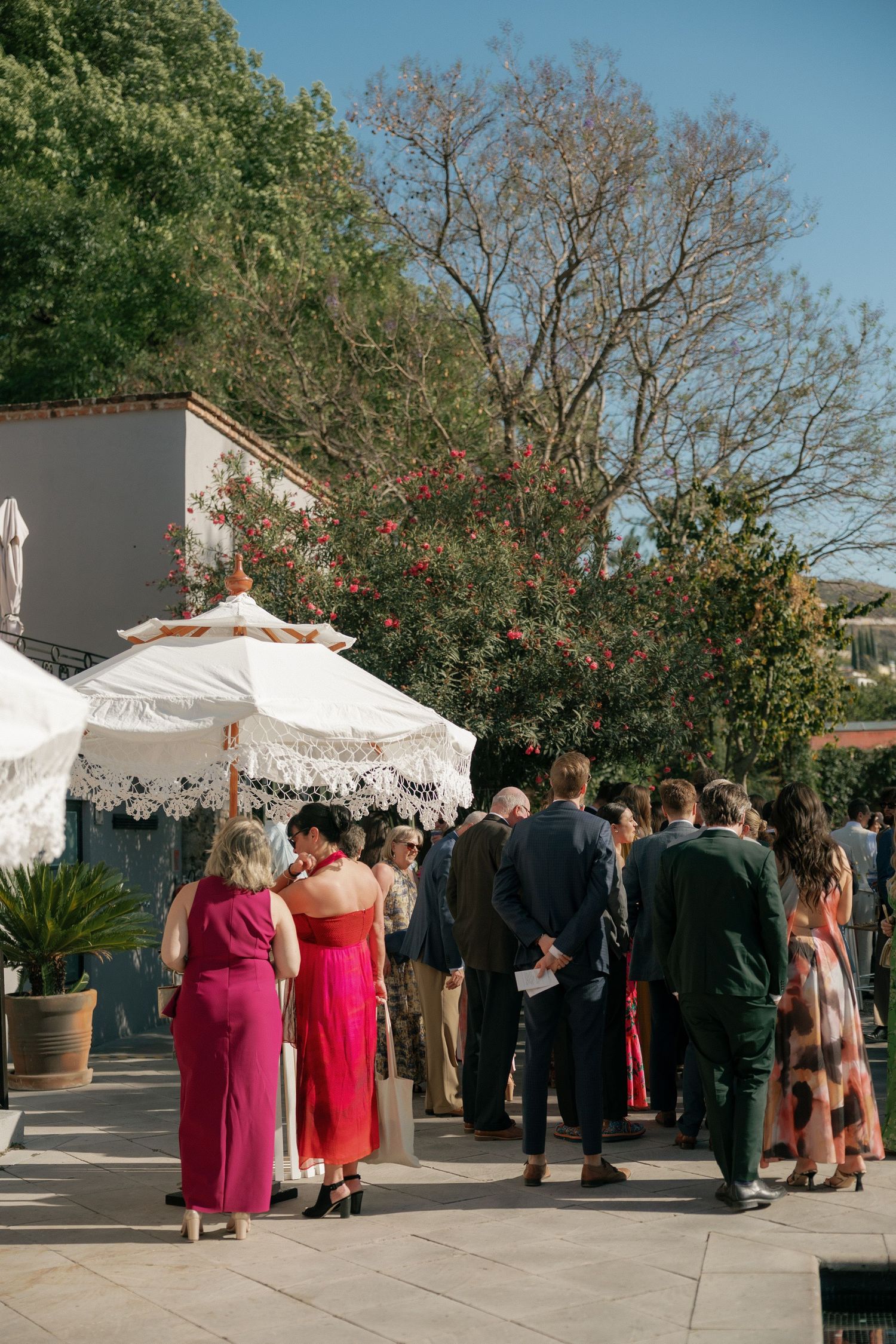 Wedding guests gather under white umbrellas at an outdoor venue.