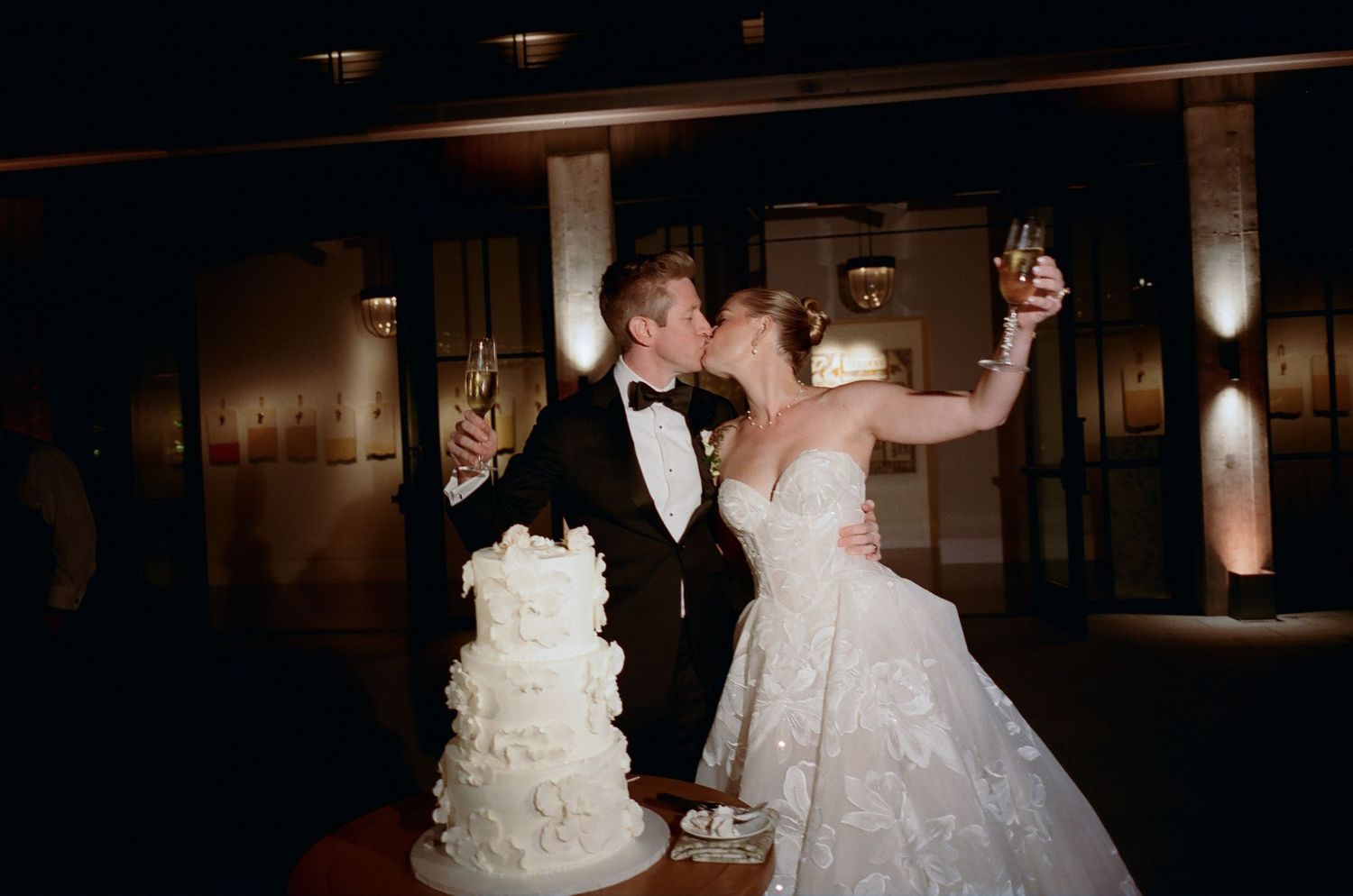 A couple celebrates next to their elegant white wedding cake at their reception.