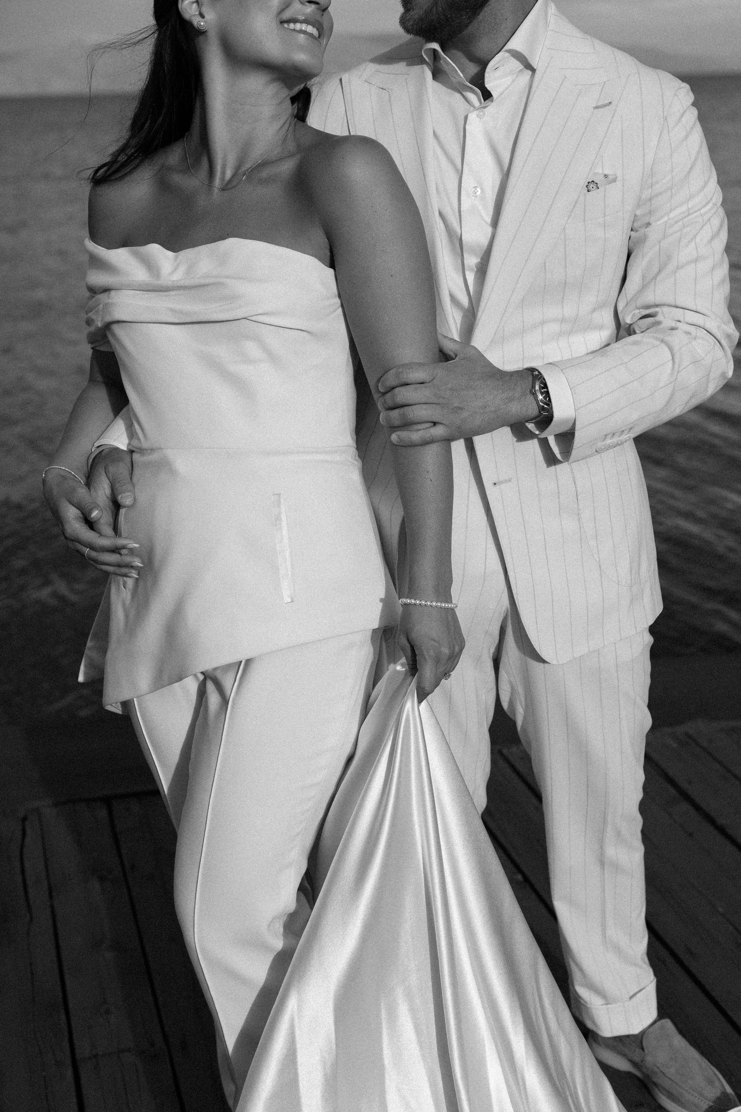 Couple in white attire share intimate moments on wooden dock at sunset.