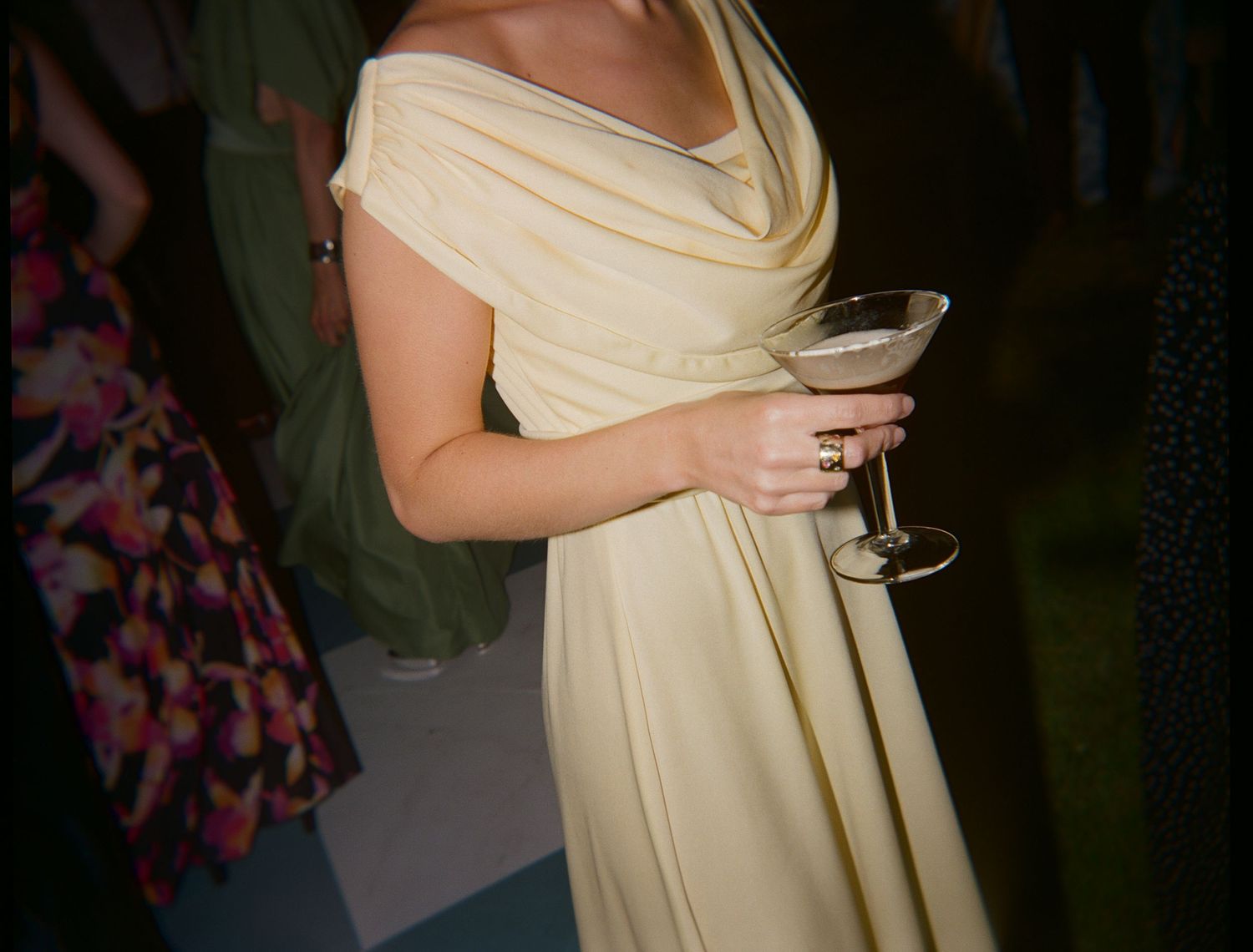 Person in cream-colored dress holding a cocktail glass at an evening event.