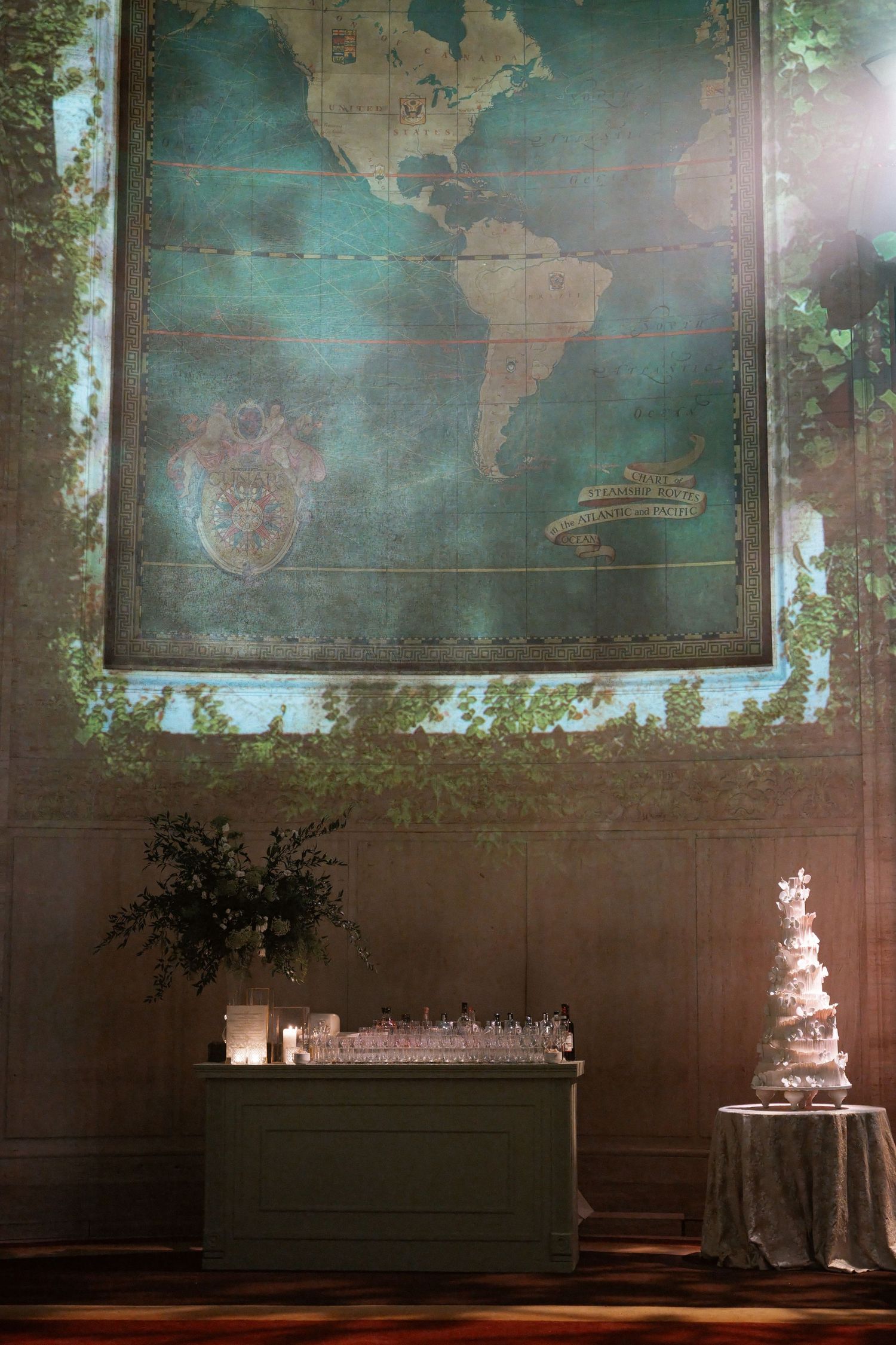 The image shows an old, weathered world map hanging on a wall, with a table and cake in the foreground.