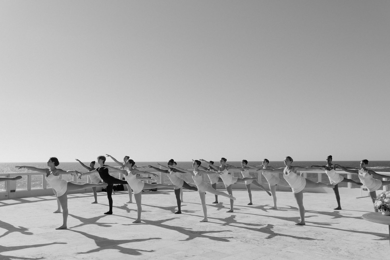 A group of people performing synchronized yoga poses on a rooftop with a scenic view.